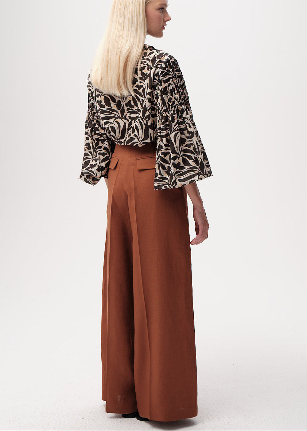 Woman wearing a patterned top and brown wide-leg pants on a white background