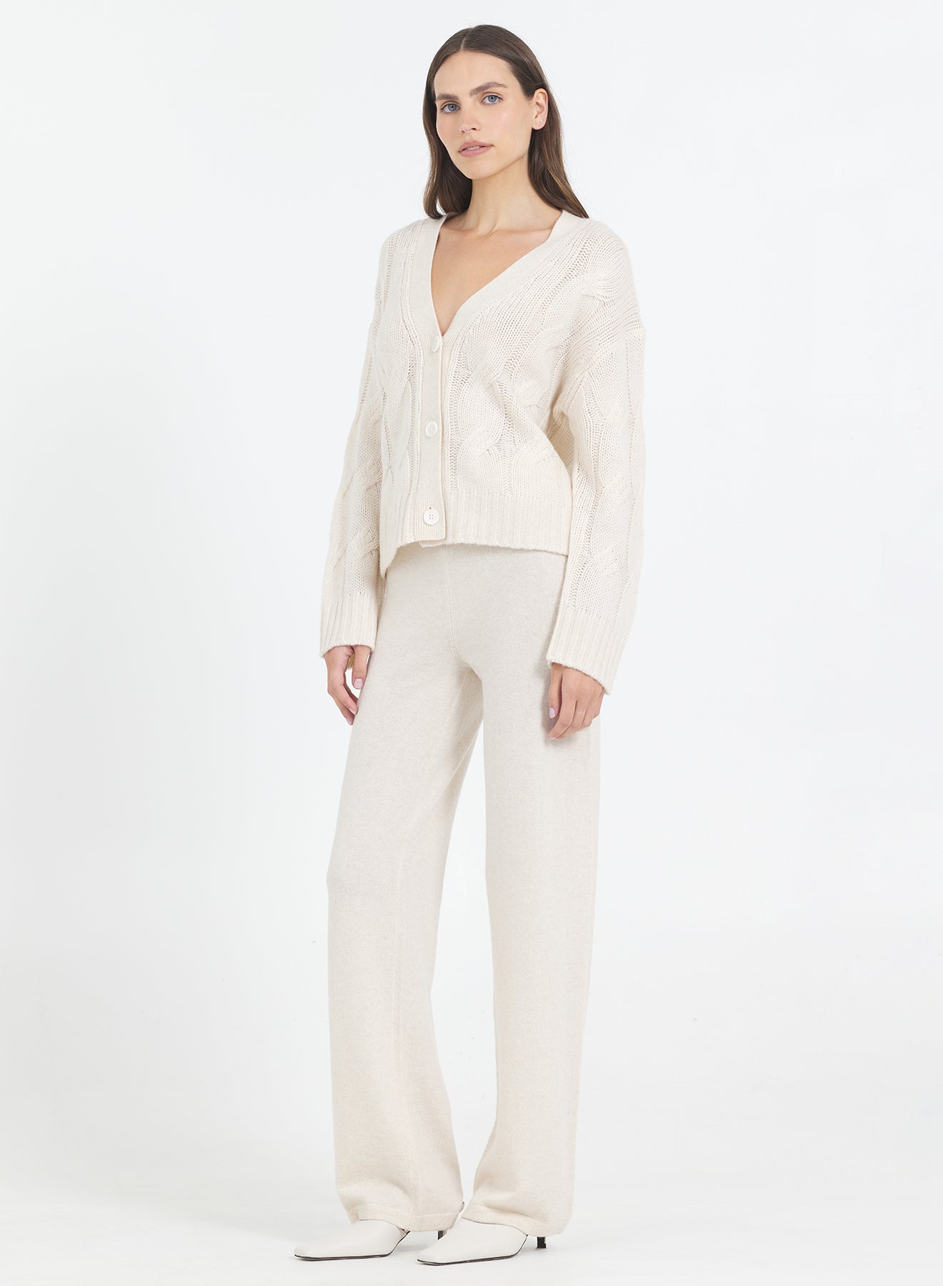 Woman wearing the One Grey Day Aster cream-colored Bone Cashmere Cable Cardigan and pants on a white background