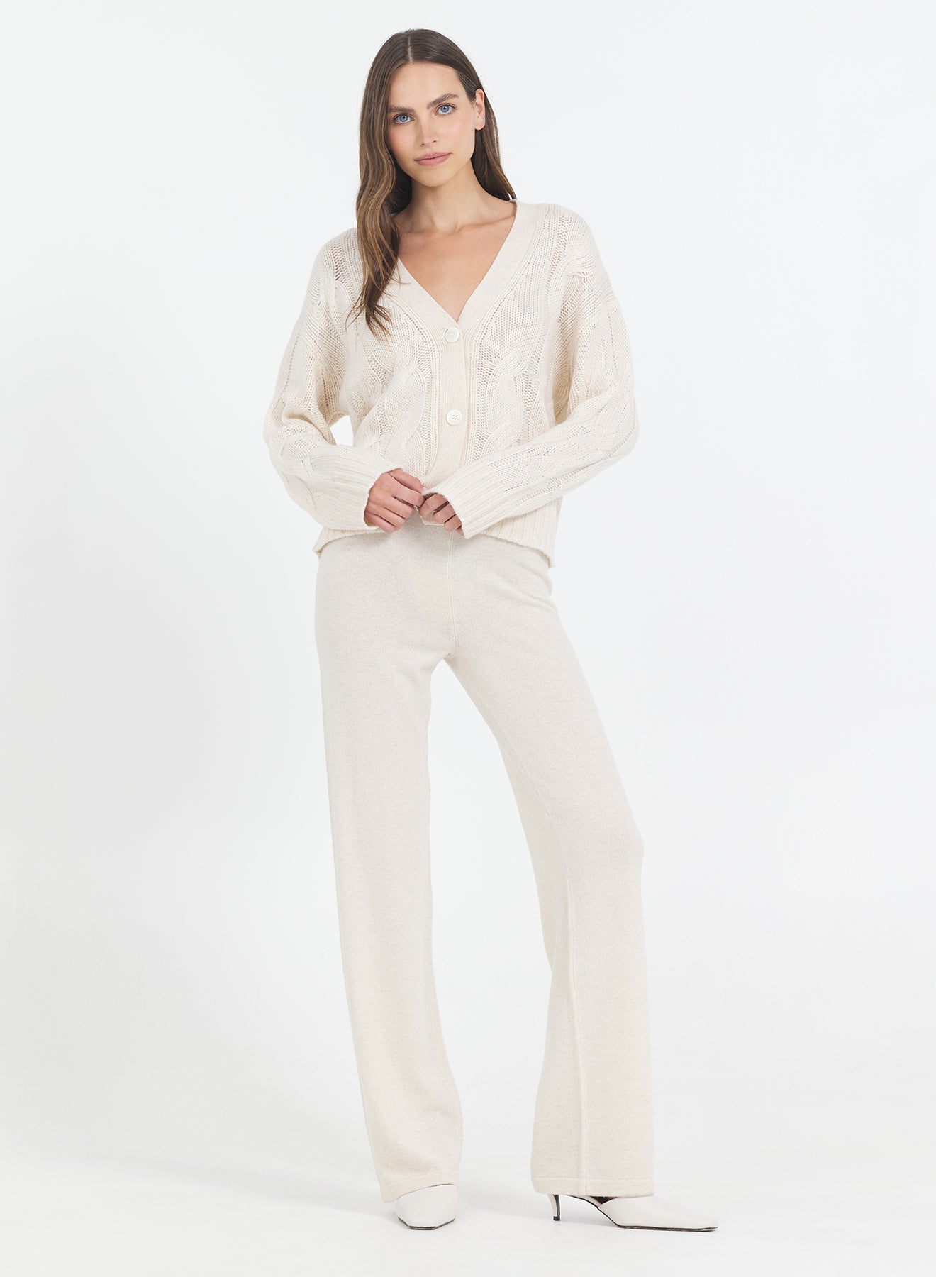 Woman wearing the One Grey Day Aster cream-colored Bone Cashmere Cable Cardigan and pants on a white background