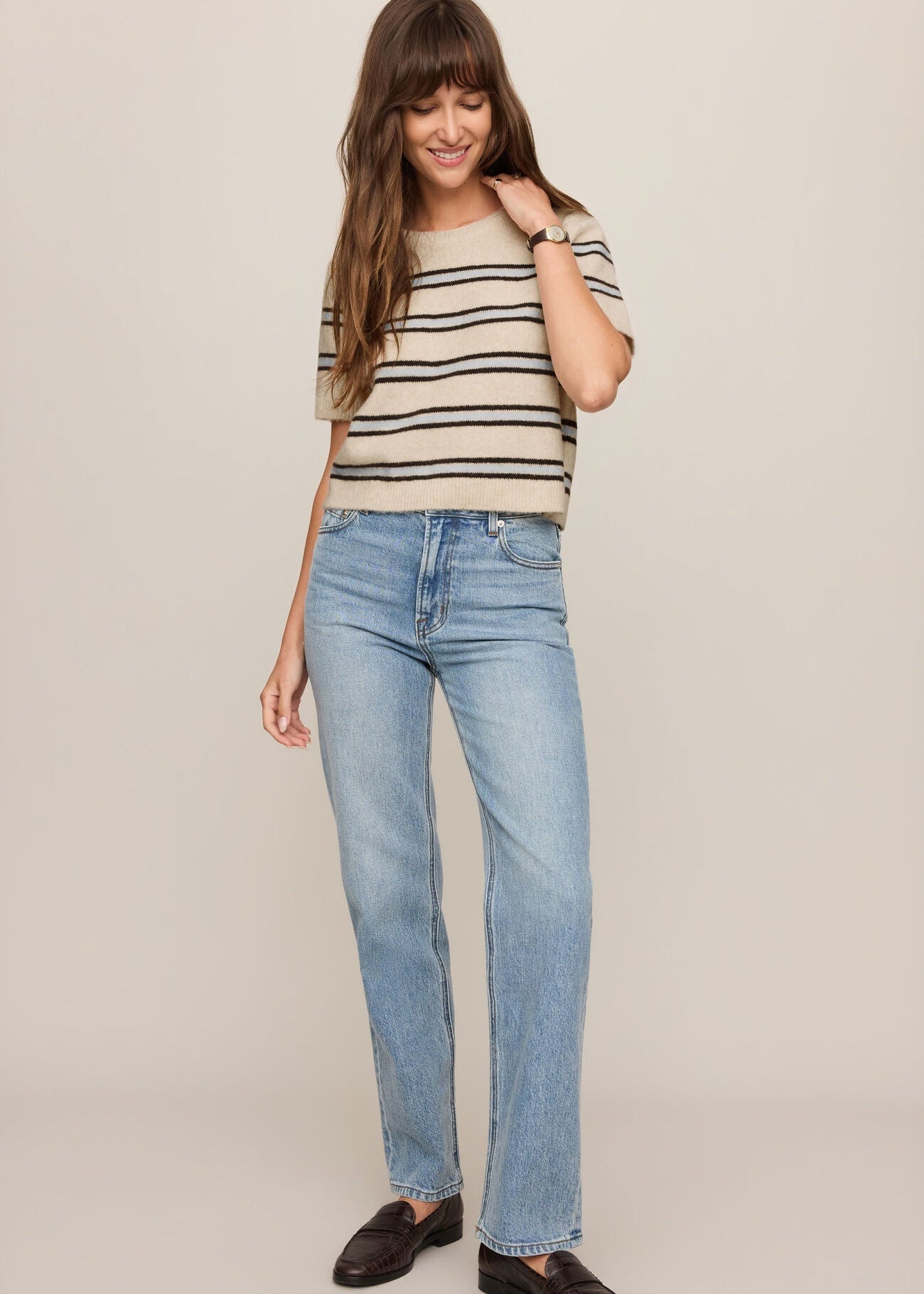 Woman wearing a striped shirt and blue jeans on a plain background