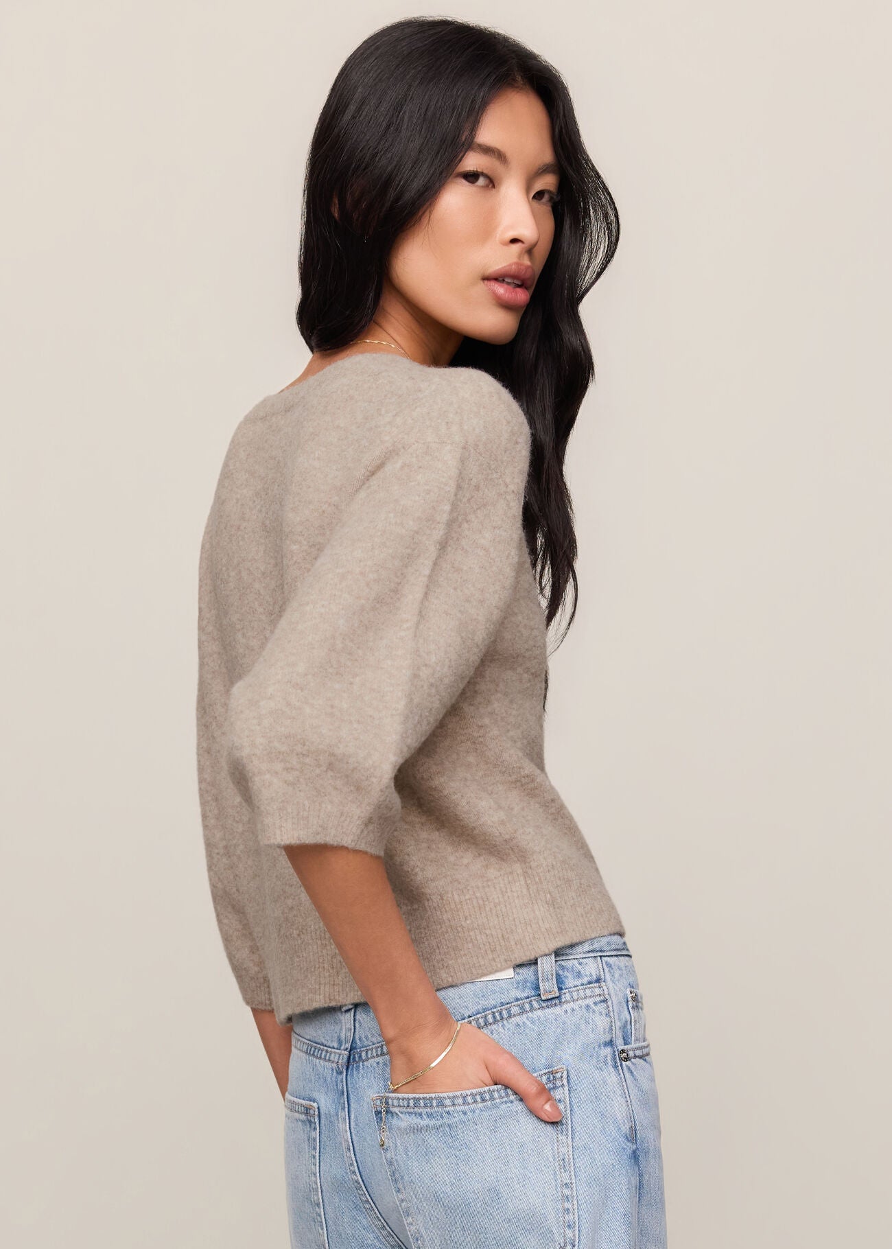Woman wearing a beige sweater and light blue jeans against a plain background