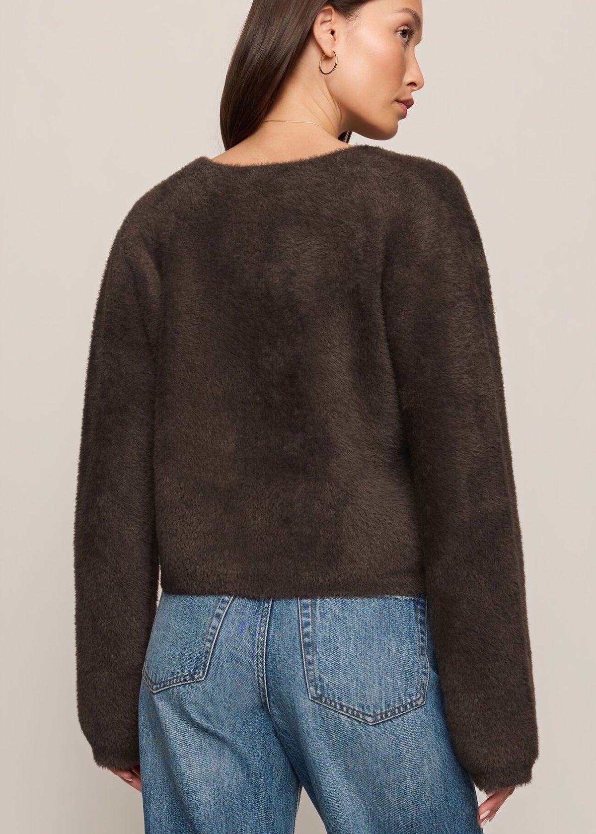Woman wearing a brown sweater and blue jeans against a plain background