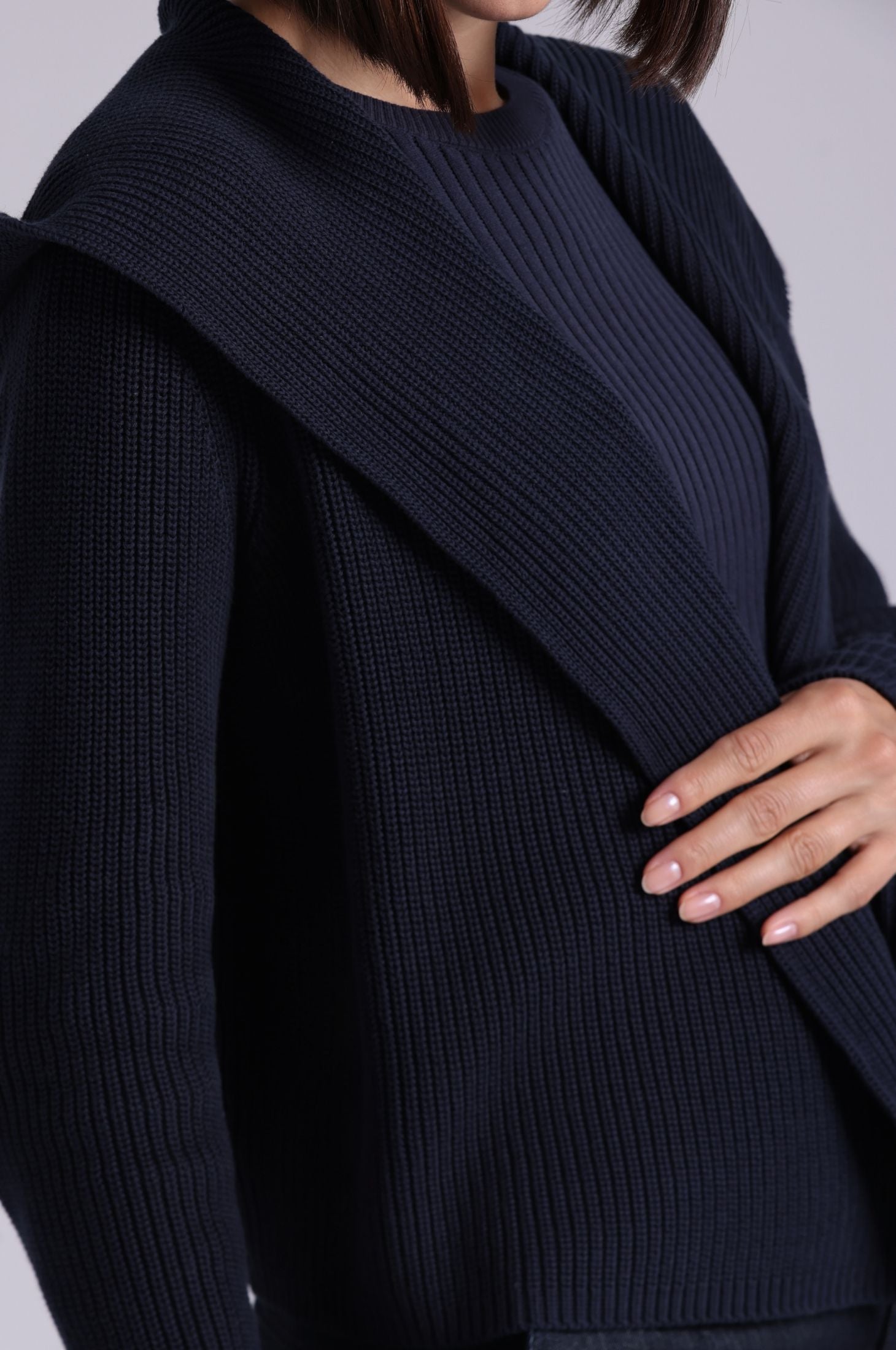 Person wearing a dark blue ribbed sweater with a hood on a light gray background
