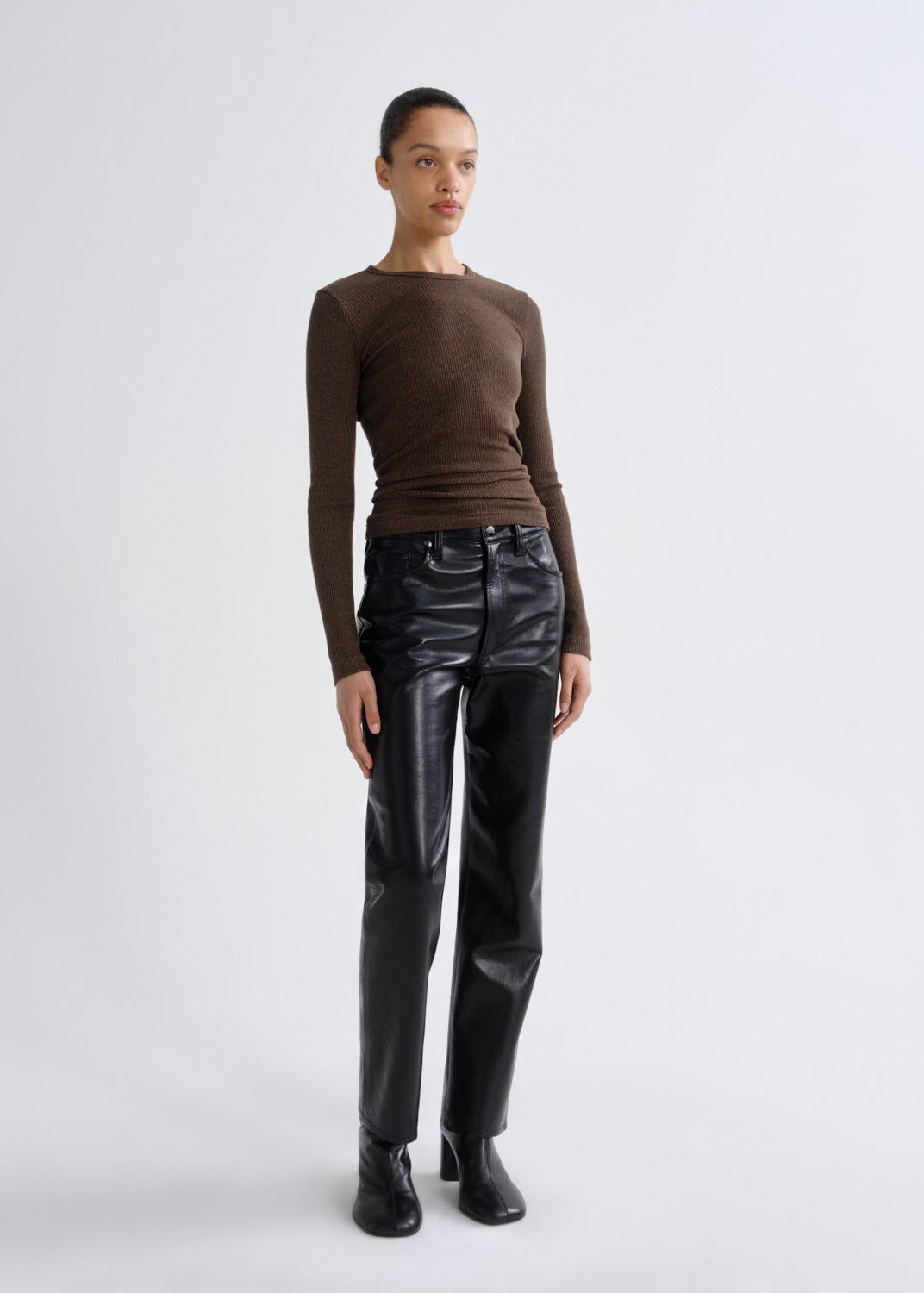 Person wearing a brown long-sleeve top and black leather pants on a white background