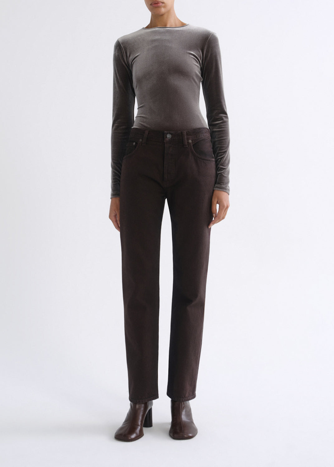 A model wearing a dark brown straight-leg pair of jeans, a dark gray long-sleeve top, and dark brown leather ankle boots, standing against a plain white studio background.