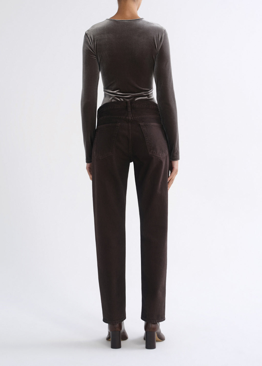 A model viewed from the back wearing a dark brown long-sleeve velvet top and matching dark brown trousers, paired with dark brown block-heeled boots, against a plain white studio background.