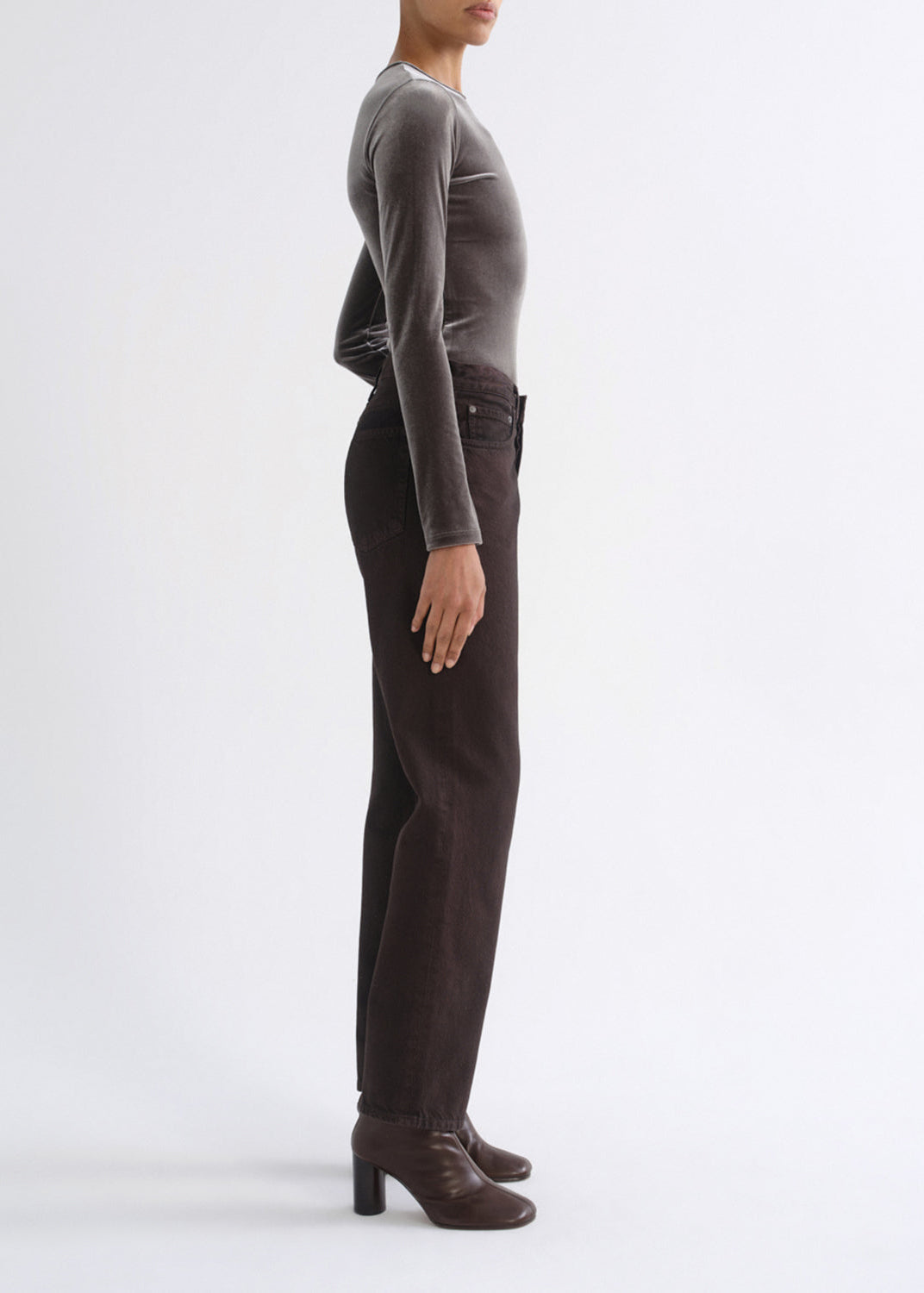 A model shown in profile wearing dark brown straight-leg corduroy pants, a dark gray long-sleeve top, and dark brown leather ankle boots against a plain white studio background.