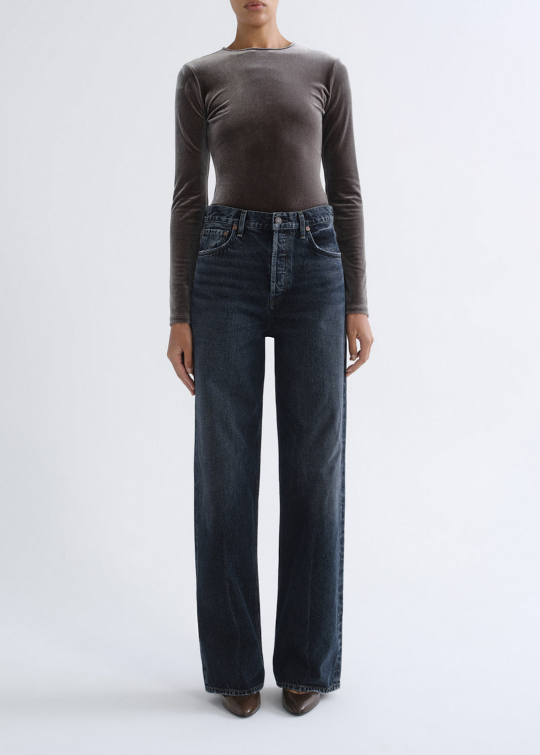 A model wearing a dark brown long-sleeve top and dark blue wide-leg jeans, standing against a plain light gray studio background.