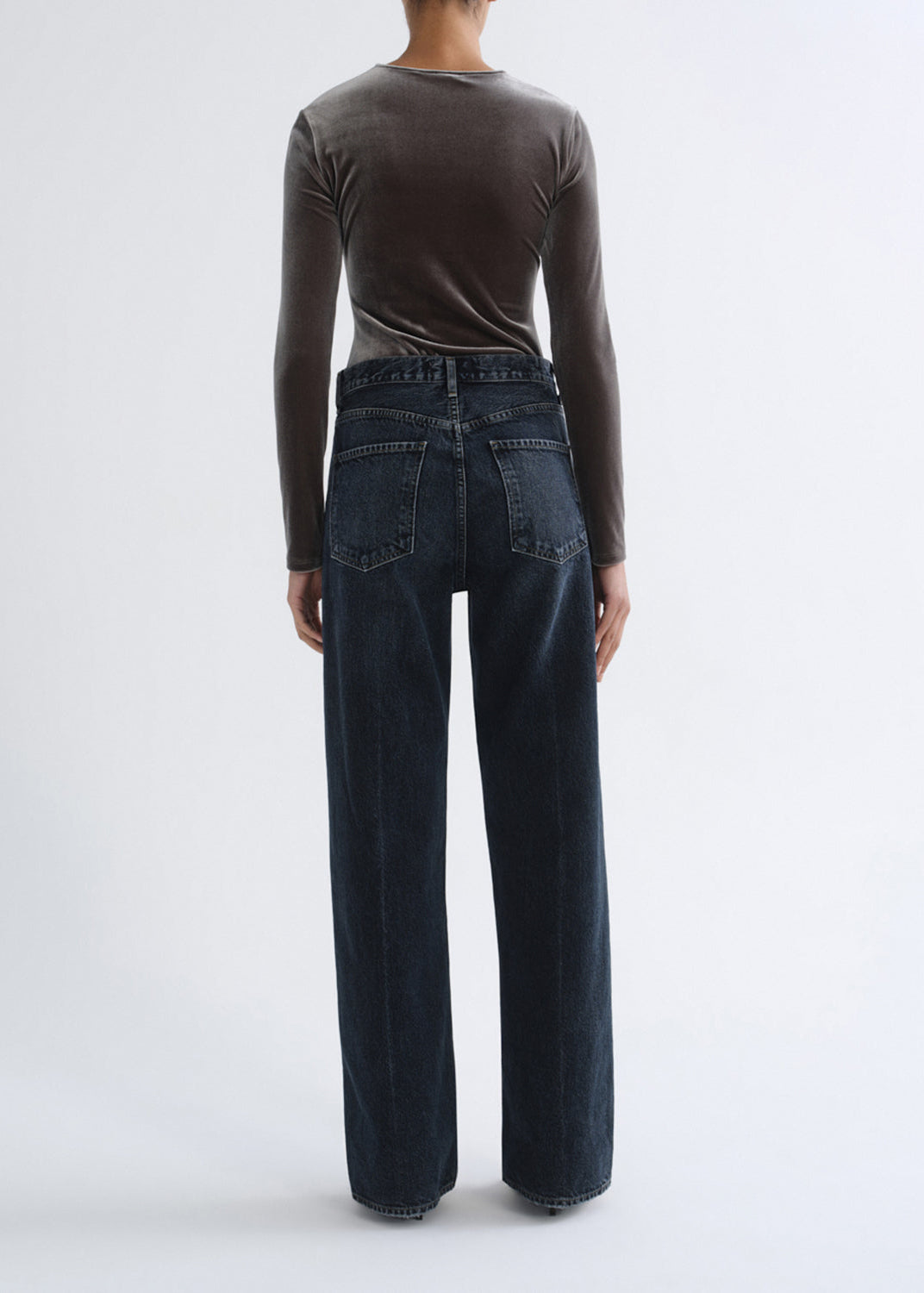 A model shown from the back wearing a dark brown long-sleeve top and dark wide-leg denim jeans against a plain white studio background.