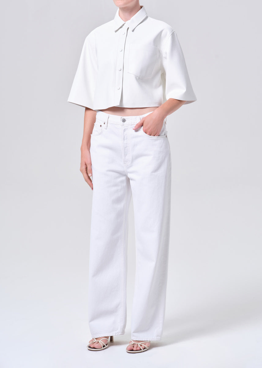 Person wearing a white cropped shirt and white pants on a light gray background