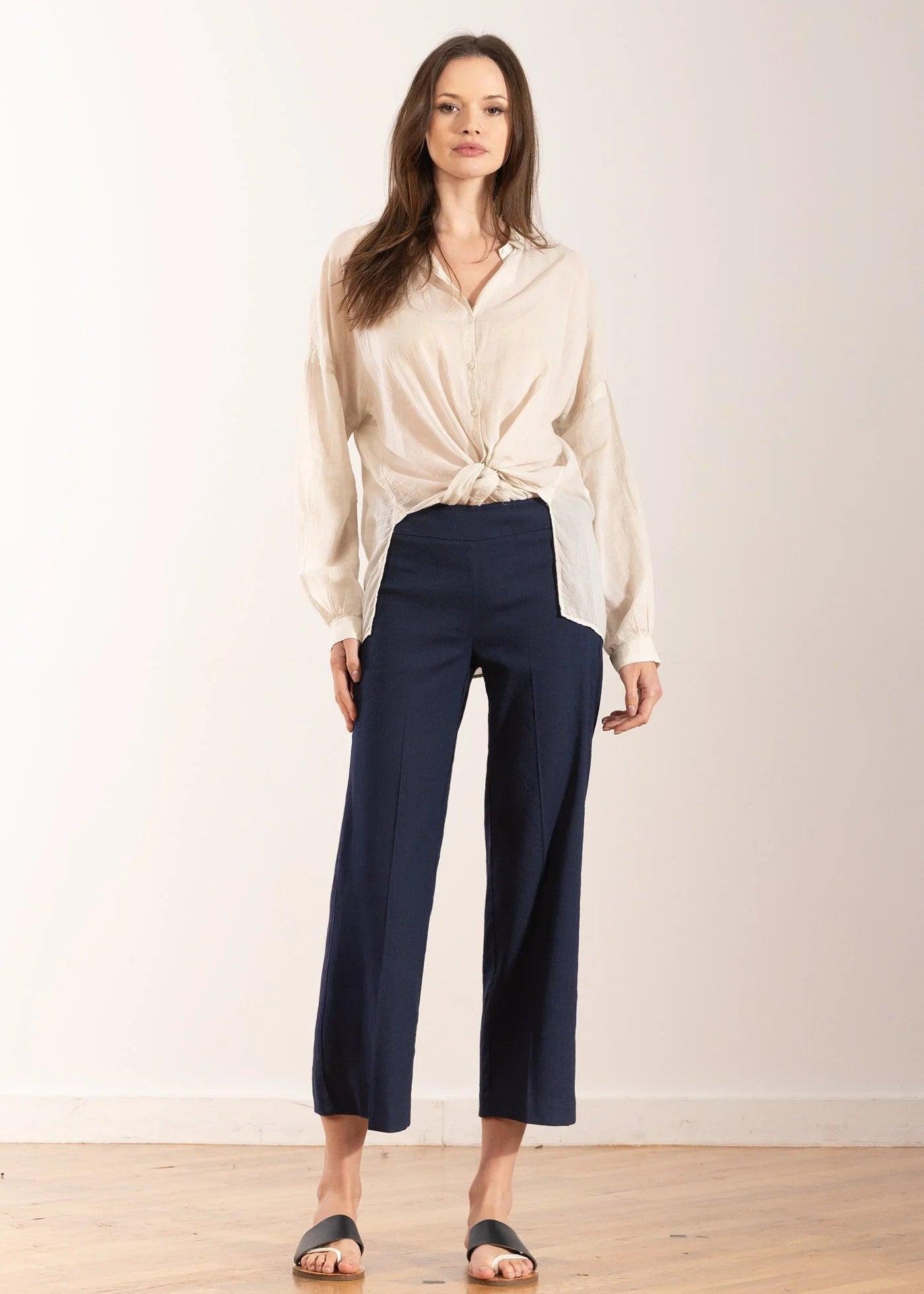 Woman wearing a white blouse and navy pants against a plain background