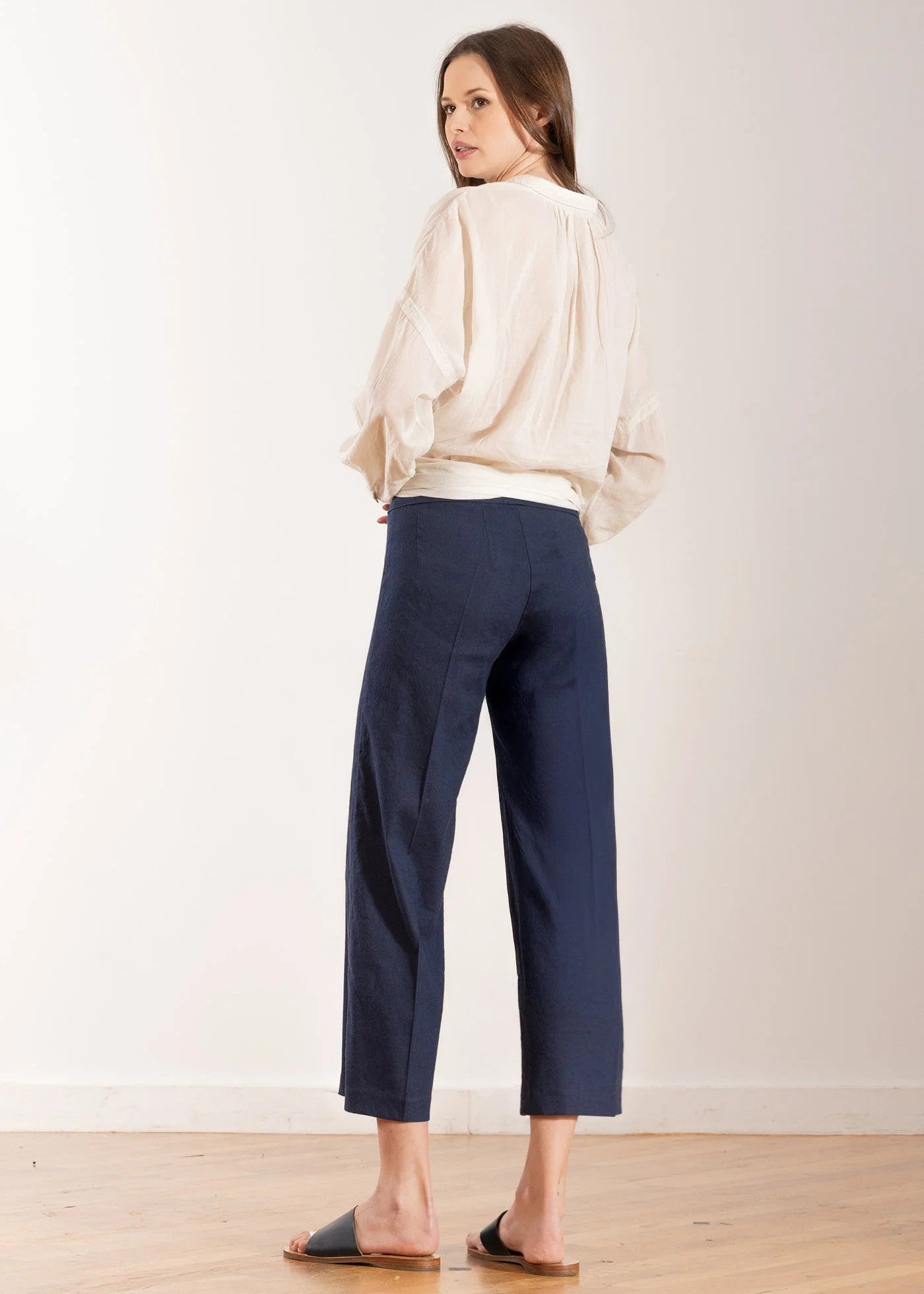Woman wearing a cream blouse and navy pants against a white background