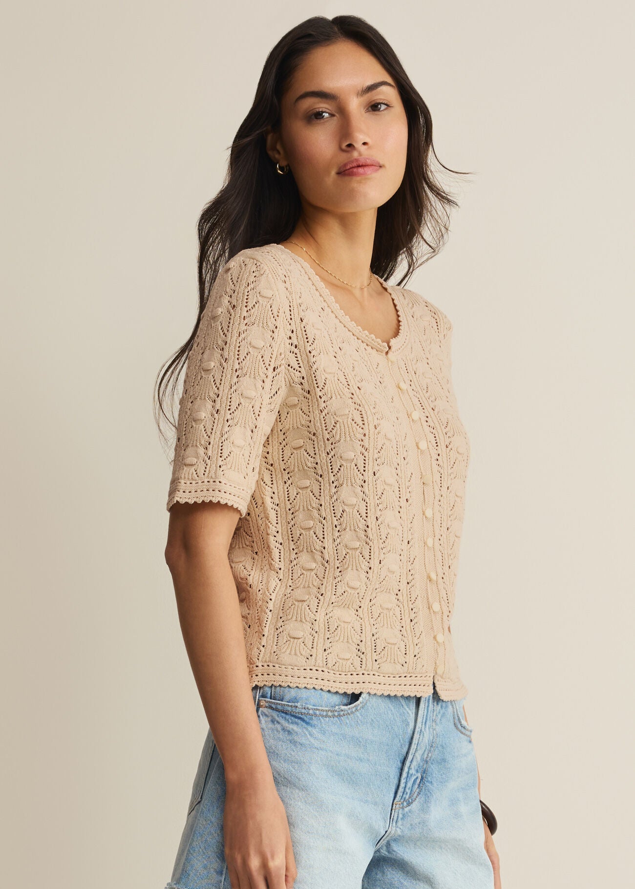 Woman wearing a beige lace top and denim shorts against a neutral background