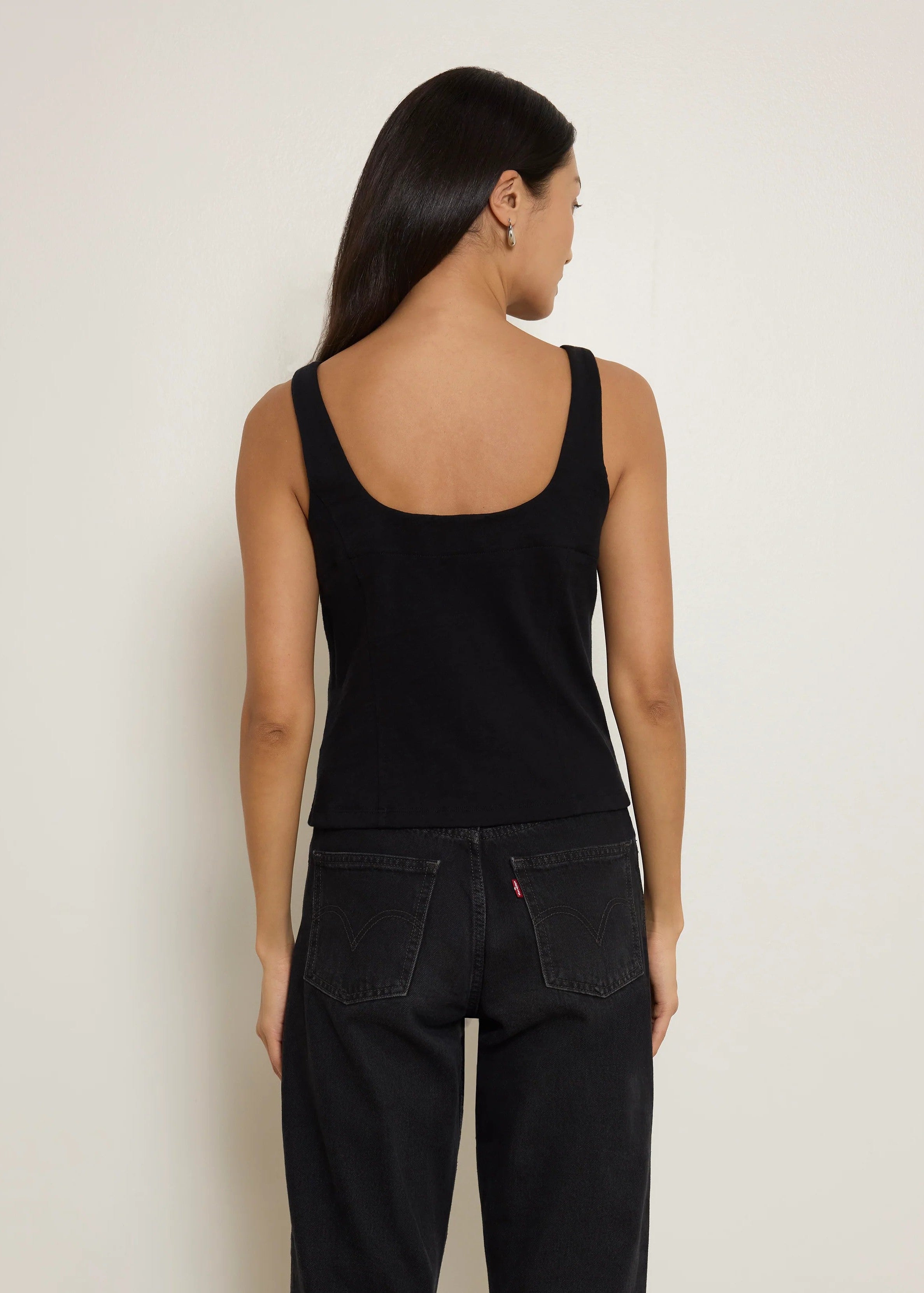 Woman wearing a black tank top and dark jeans against a plain background