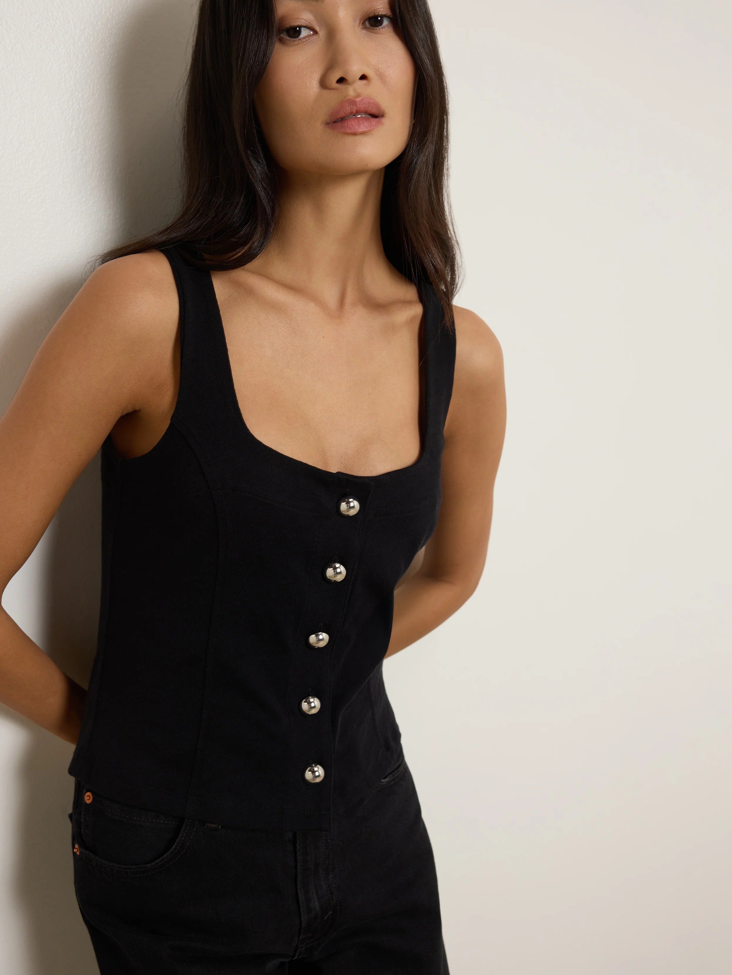 Woman wearing a black sleeveless top with buttons against a plain background