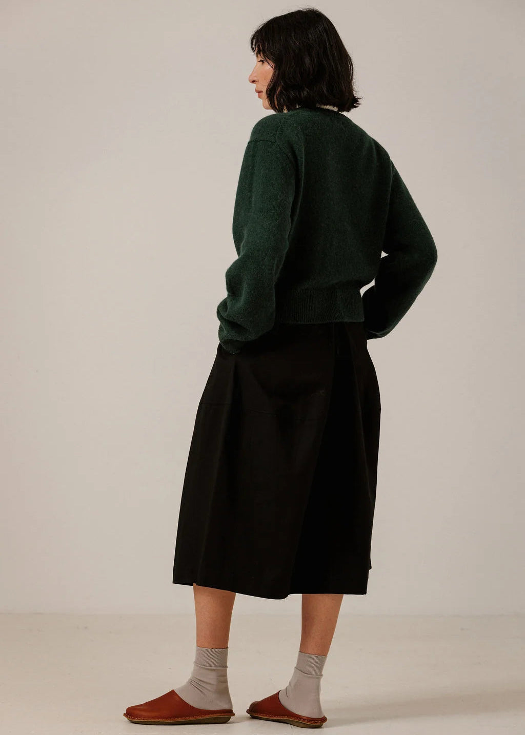 Person wearing a dark green sweater and black skirt on a plain background
