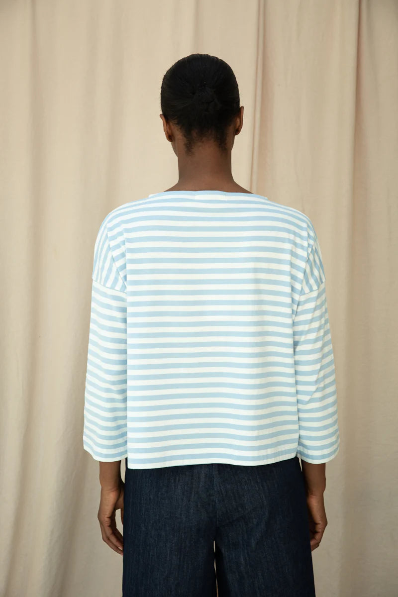Person wearing a light blue and white striped shirt against a beige curtain background