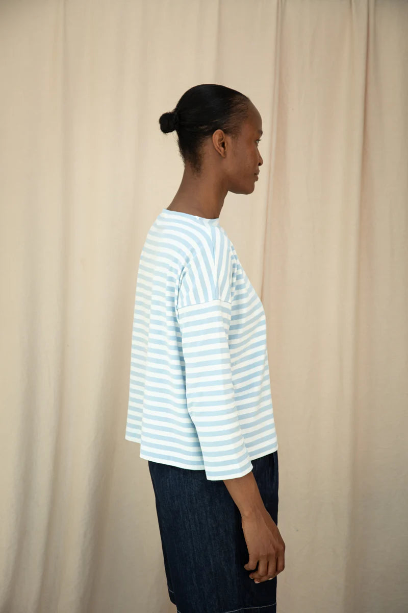 Person wearing a striped shirt against a beige curtain background
