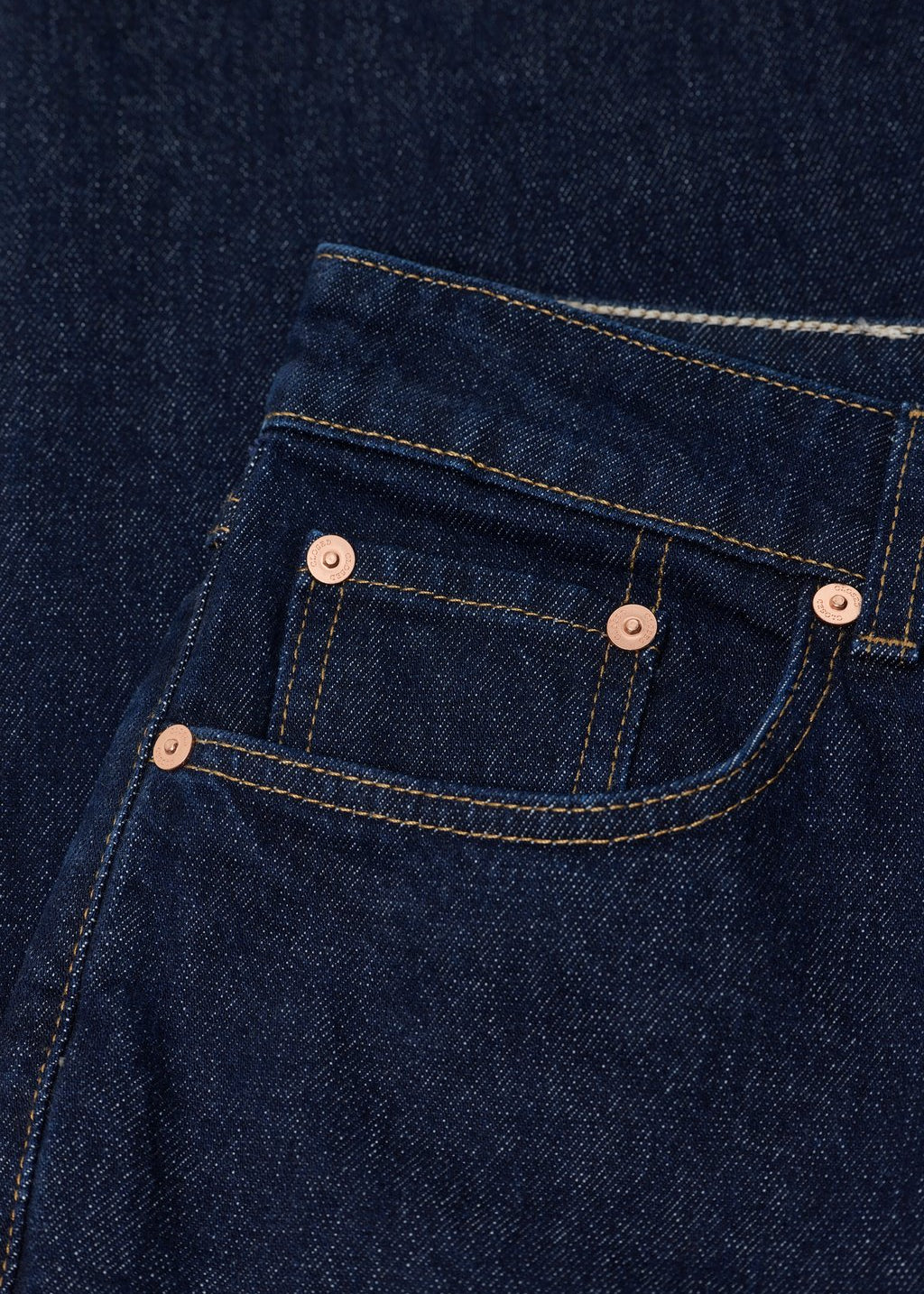 Close-up of a dark indigo denim pocket with copper-toned rivets and contrast stitching.