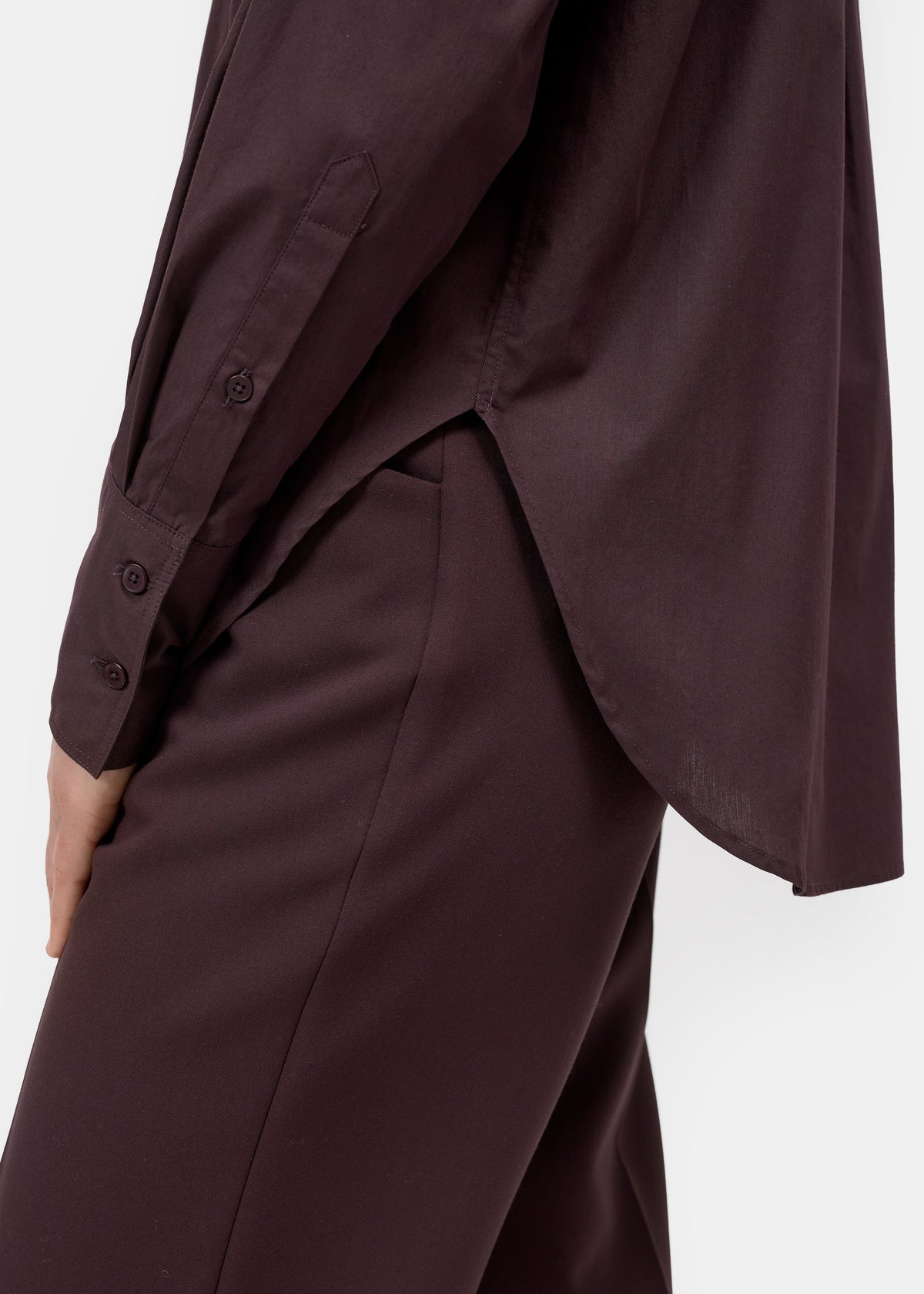 Close-up of a person wearing a dark plum button-front top and matching dark trousers against a plain light background.