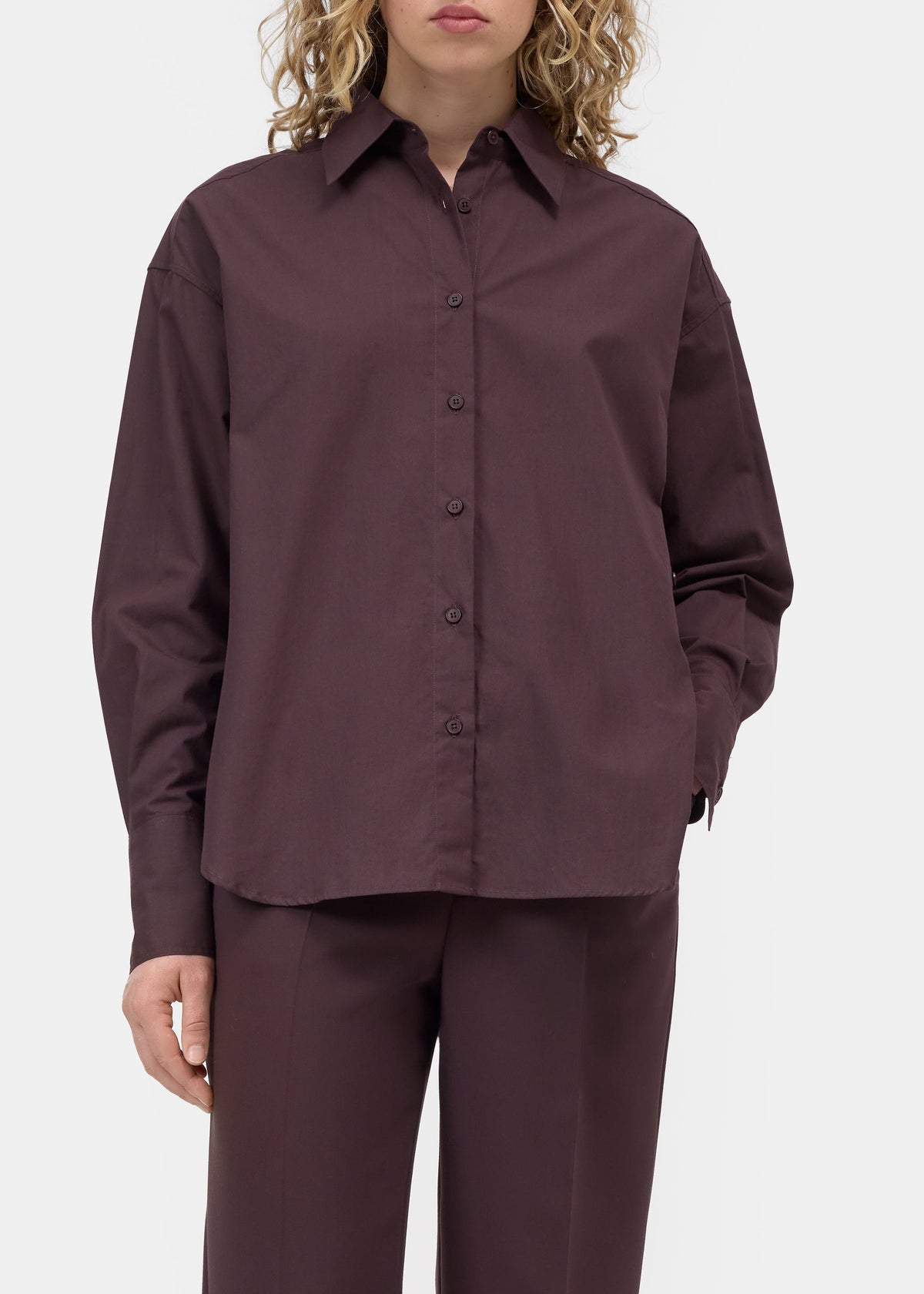 A model wearing a dark plum button-up shirt and matching trousers against a light gray studio background.