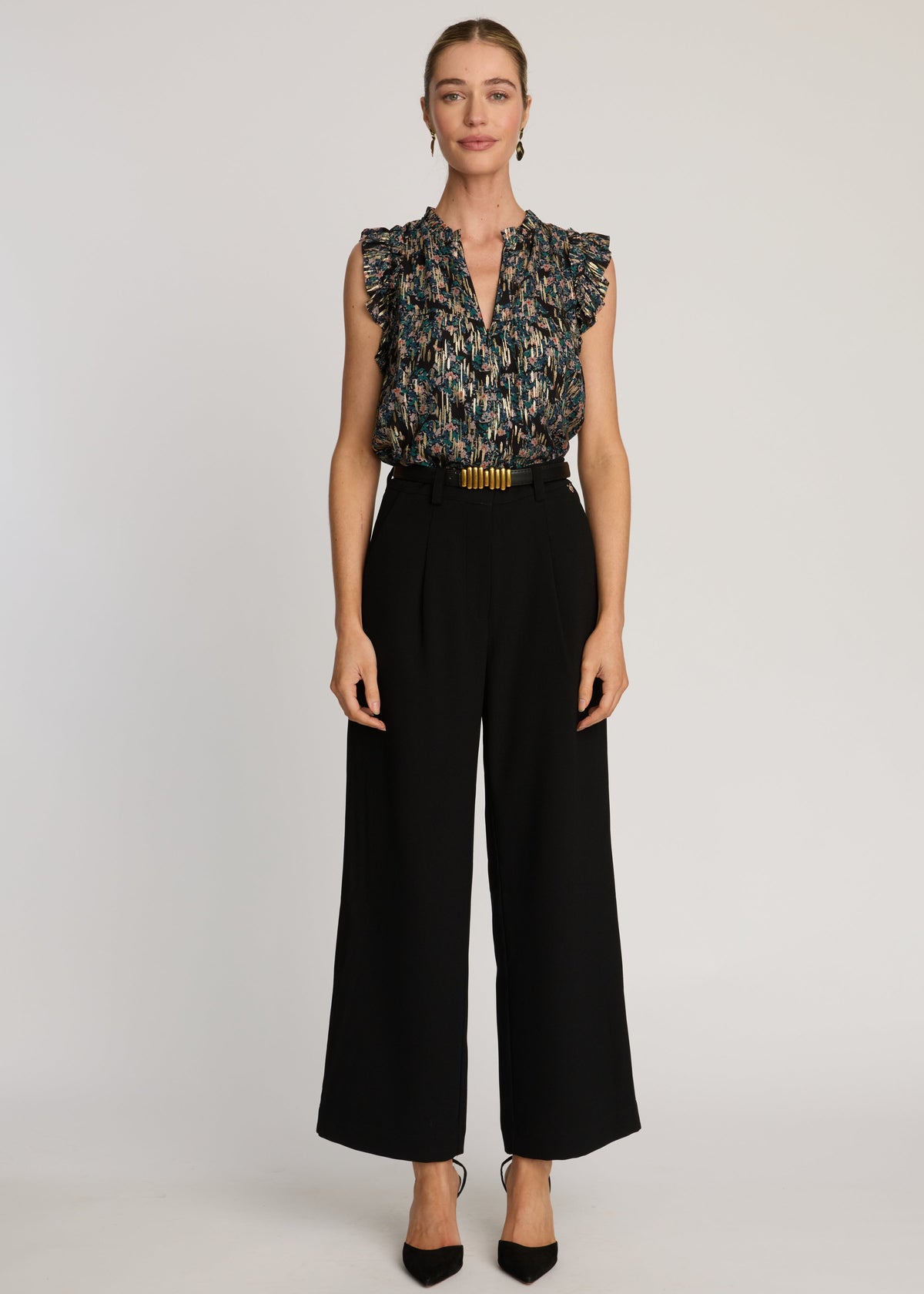Woman wearing a patterned sleeveless top and black pants on a white background