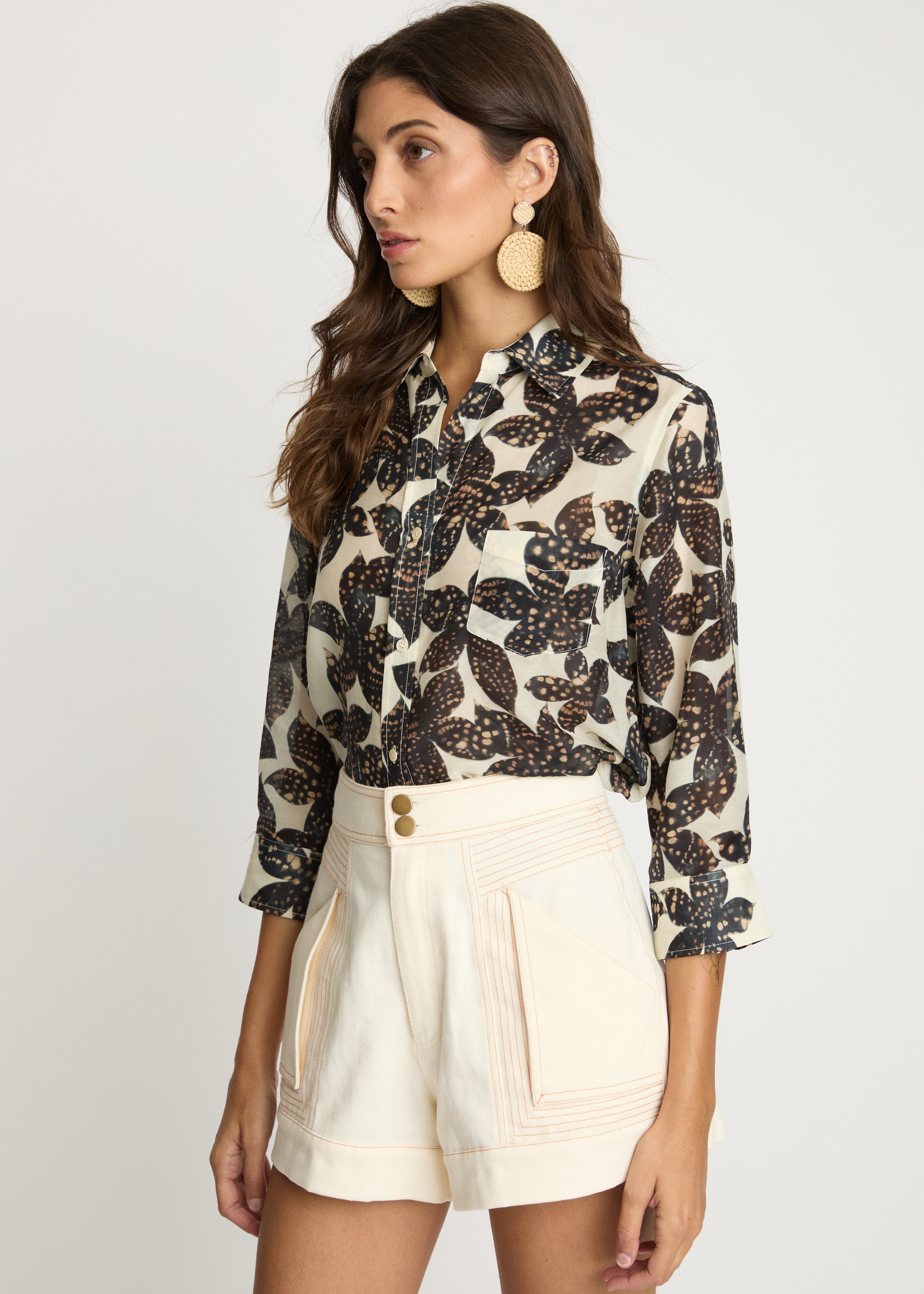 Woman wearing a patterned blouse and beige shorts on a white background