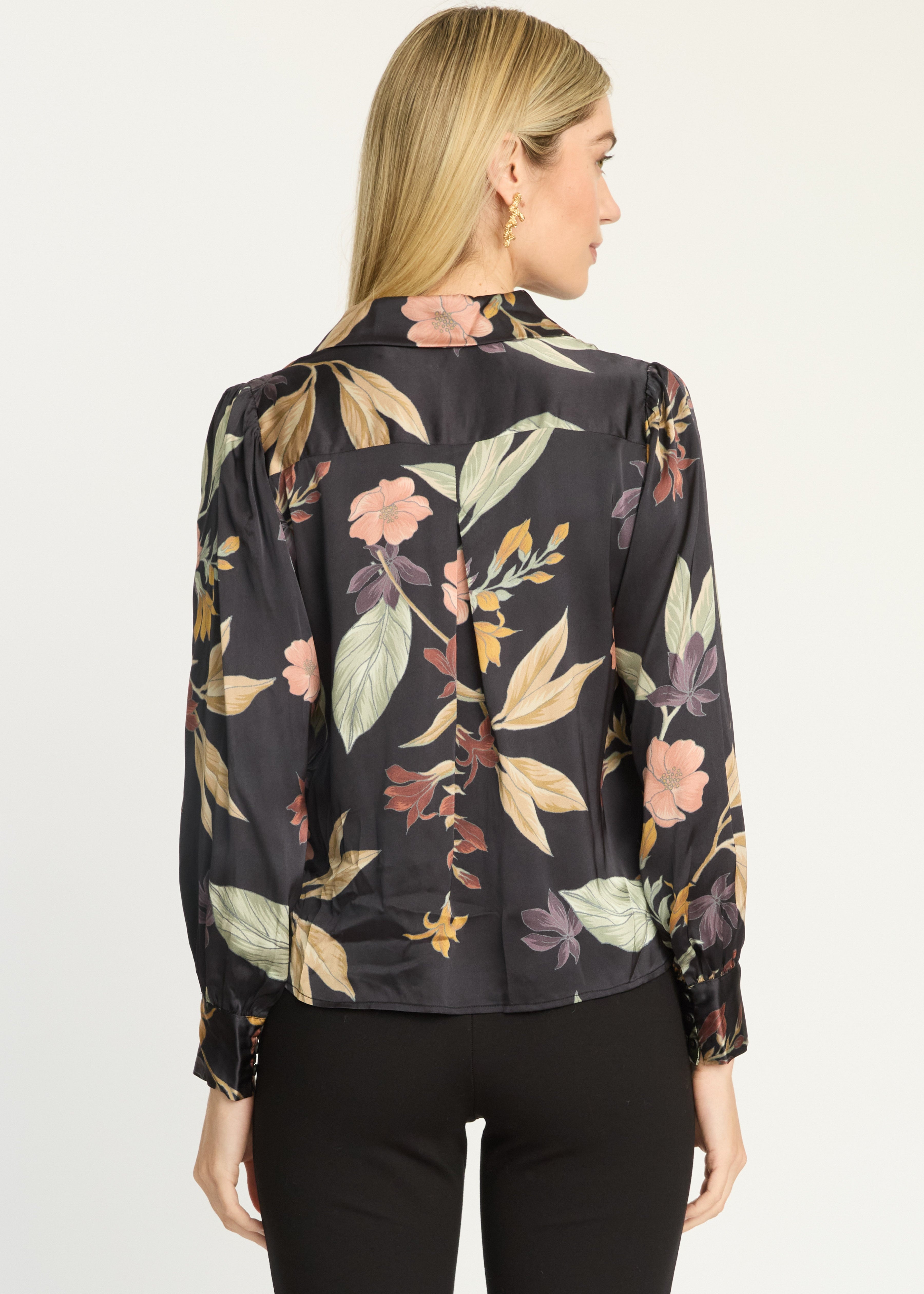 A woman shown from the back wearing a black long-sleeve blouse with a multicolor floral print and black pants, photographed against a plain light background.