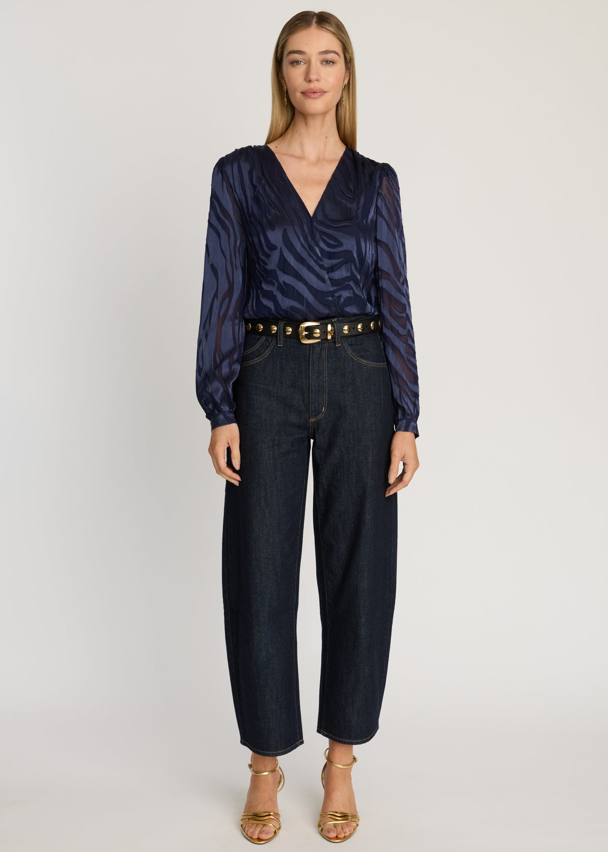 Woman wearing a navy patterned blouse and dark jeans on a white background