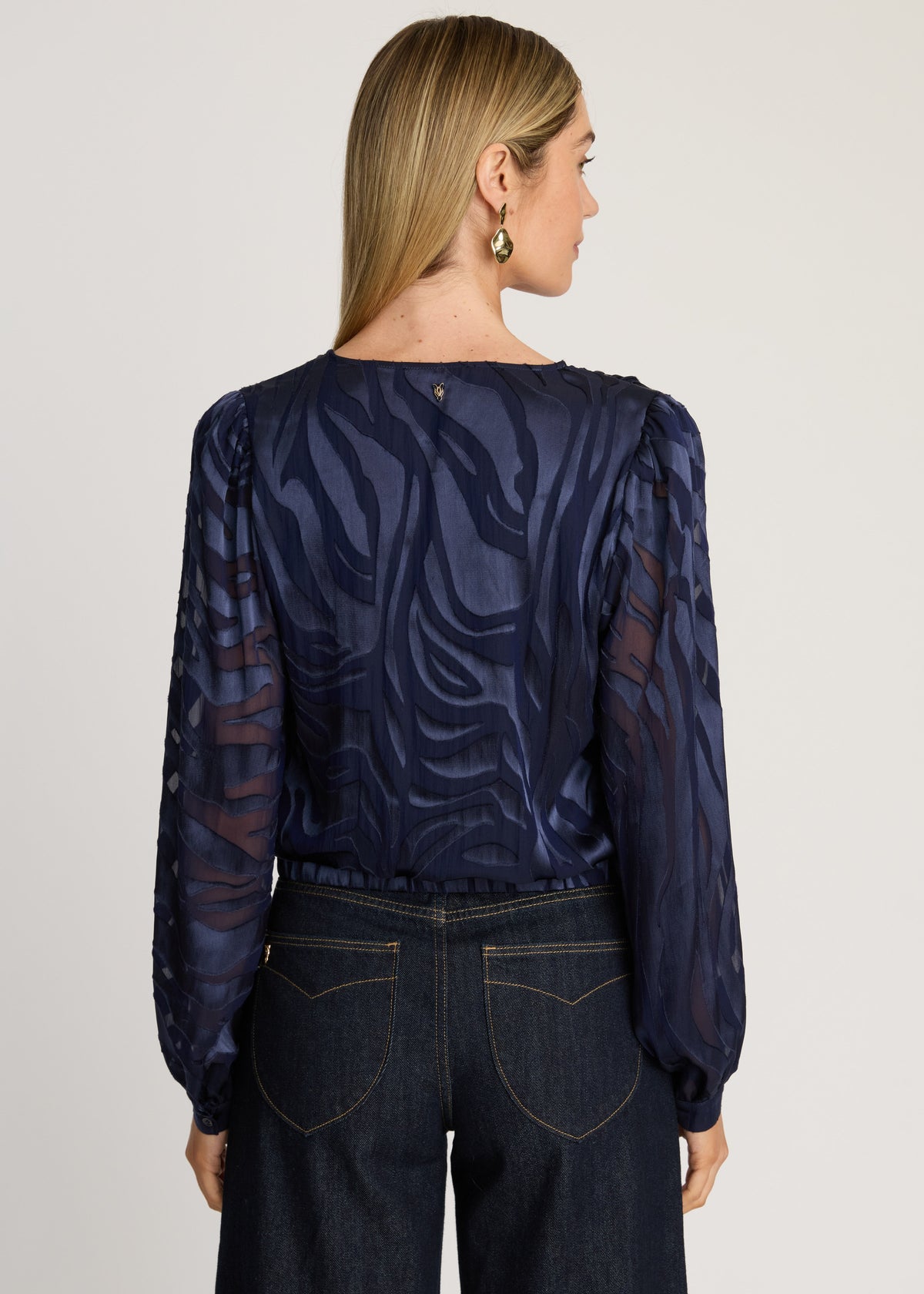 Woman wearing a dark blue patterned blouse and jeans on a plain background