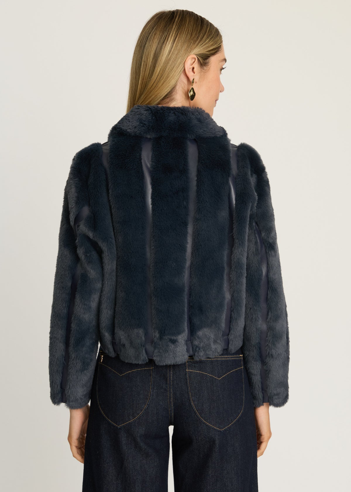 Person wearing a dark fur jacket and jeans on a plain background
