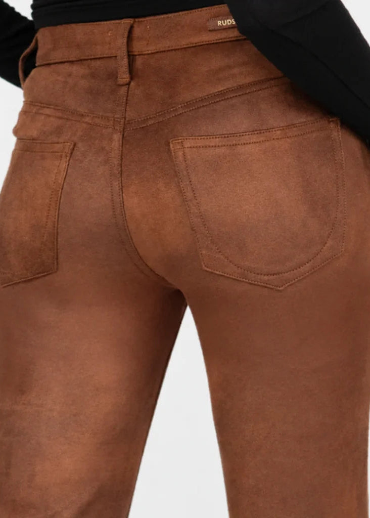 Close-up back view of a person wearing brown faux-suede pants with a black long-sleeve top, showing the waistband, belt loops, and back pockets against a light gray background.