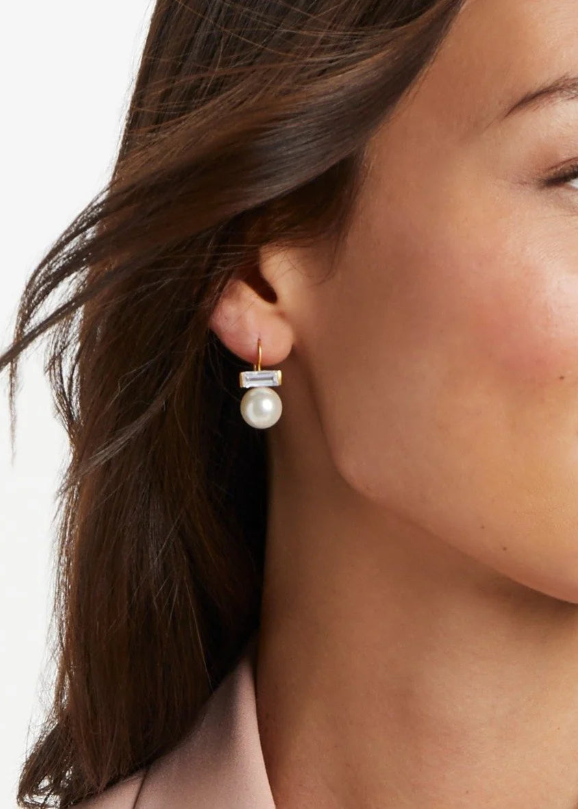 Close-up of a woman wearing pearl earrings with a neutral background