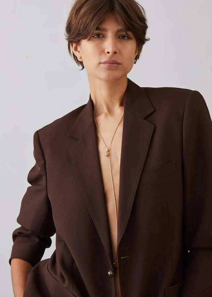 Woman wearing a brown blazer over a beige top against a plain background
