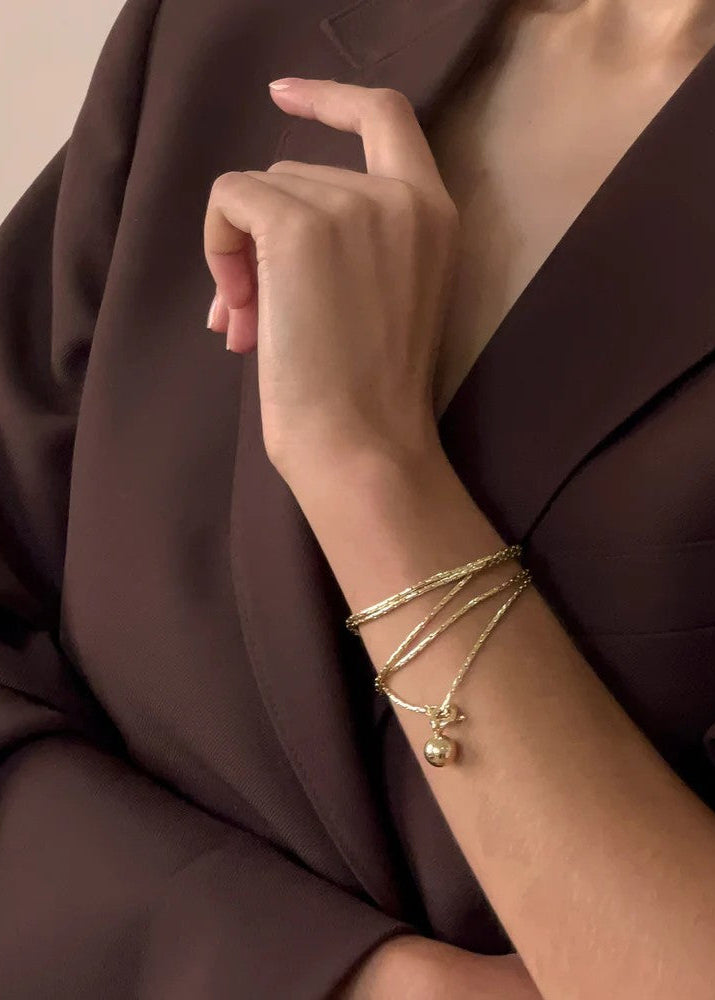Gold bracelet with a small pendant on a person's wrist against a brown background