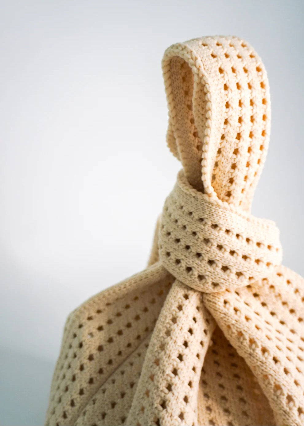 Beige knitted scarf with a knot on a light gray background