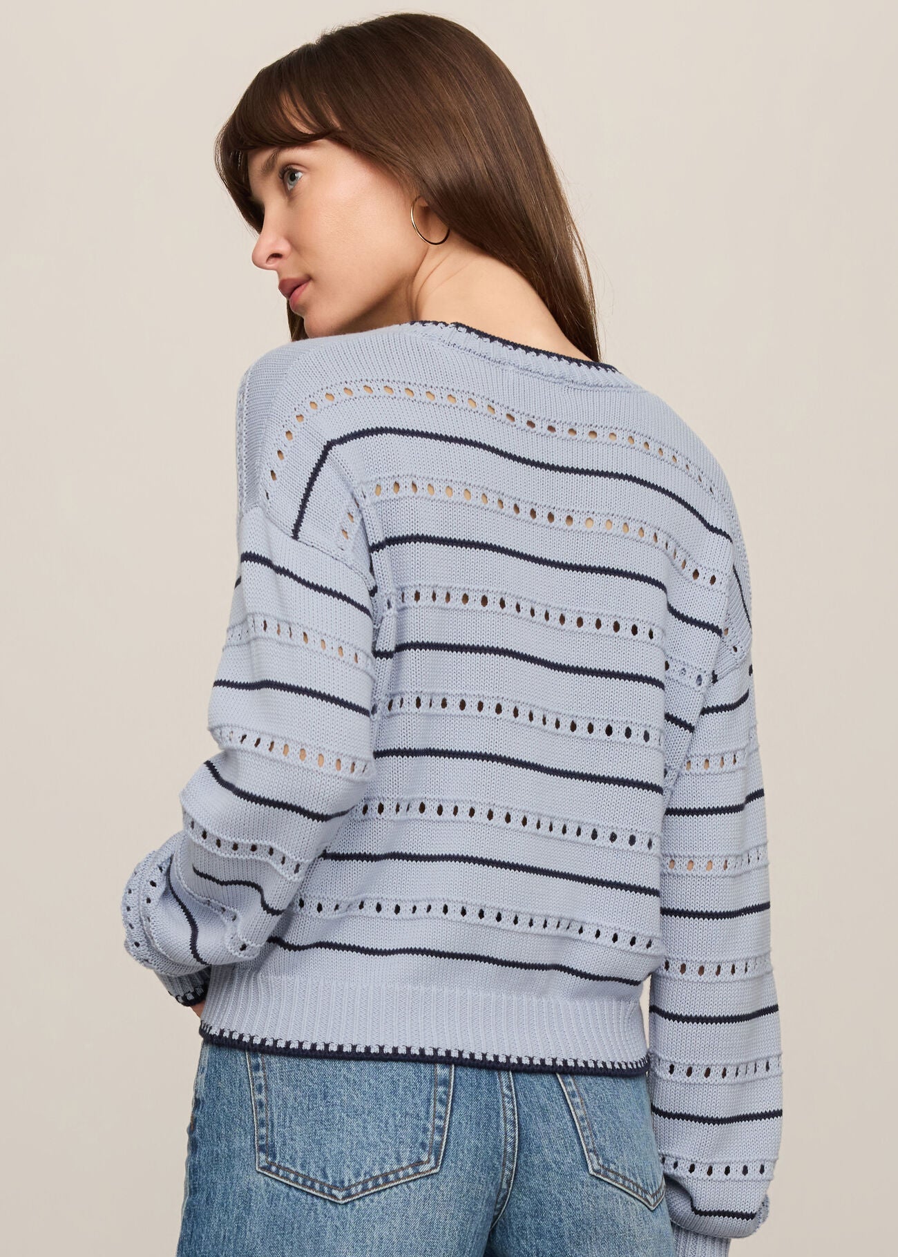 Woman wearing a light blue striped sweater and jeans on a beige background