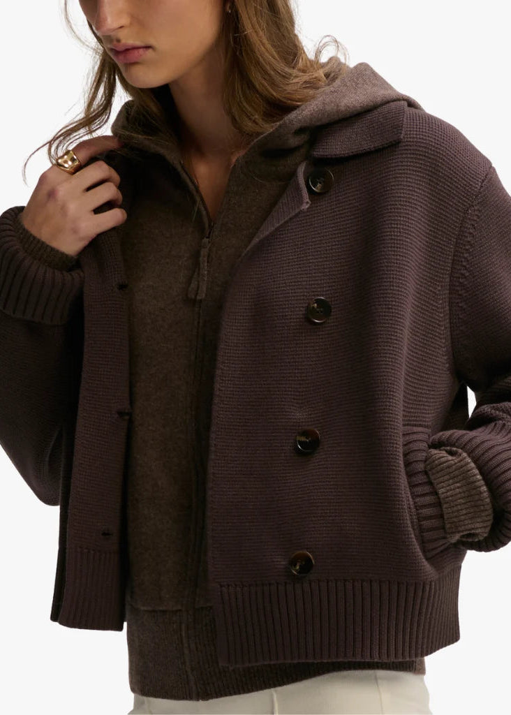 A woman wearing a dark brown ribbed knit hooded cardigan with large dark buttons over a matching brown zip-up sweater, shown against a plain light background.