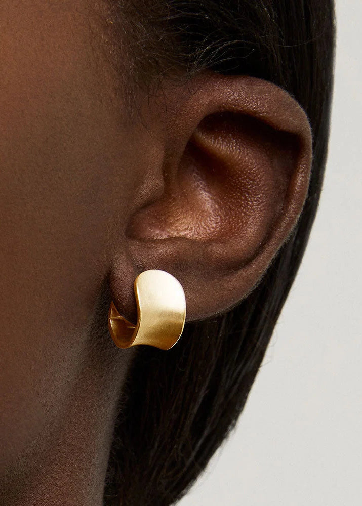 Gold hoop earring worn by a person with a neutral background