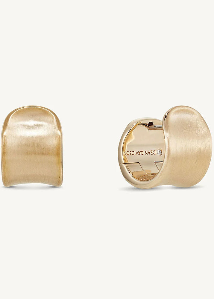 A pair of gold-toned hoop earrings shown on a clean off-white background, with one earring facing forward and the other turned to show the interior clasp.