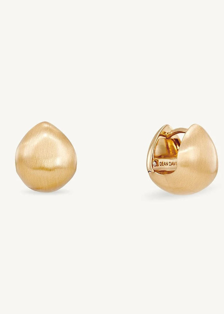 A pair of gold huggie hoop earrings, one shown from the front with a brushed finish and the other from the side displaying the clasp mechanism. The earrings are displayed on a clean, solid off-white background.