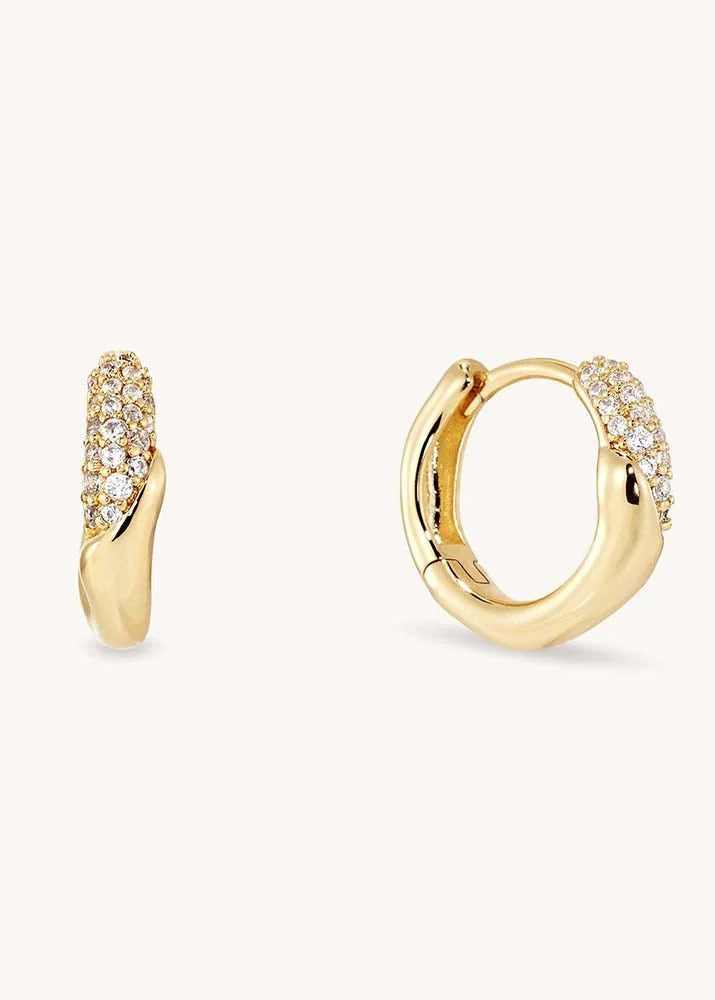 A pair of gold huggie hoop earrings with pavé-set clear stones along the front curve, shown on a clean off-white background.
