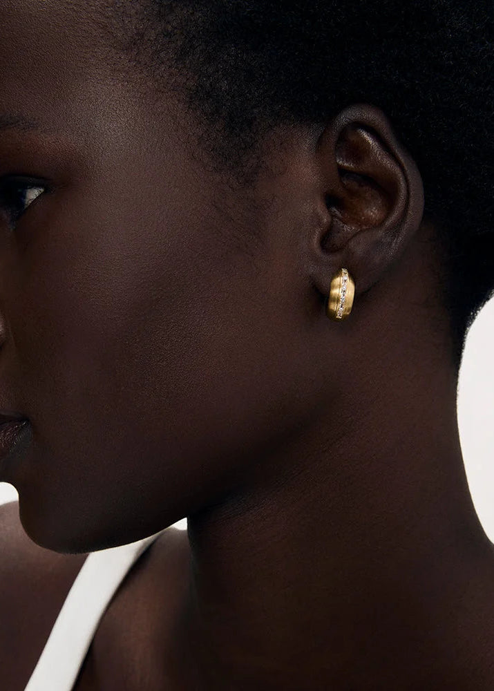 A close-up side profile of a model wearing a single silver-toned, textured stud earring against a plain light background.