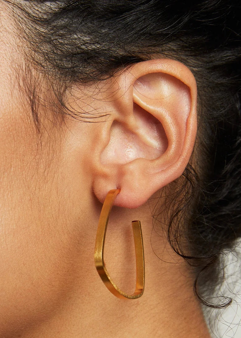 Close-up of an ear wearing a gold hoop earring with blurred background