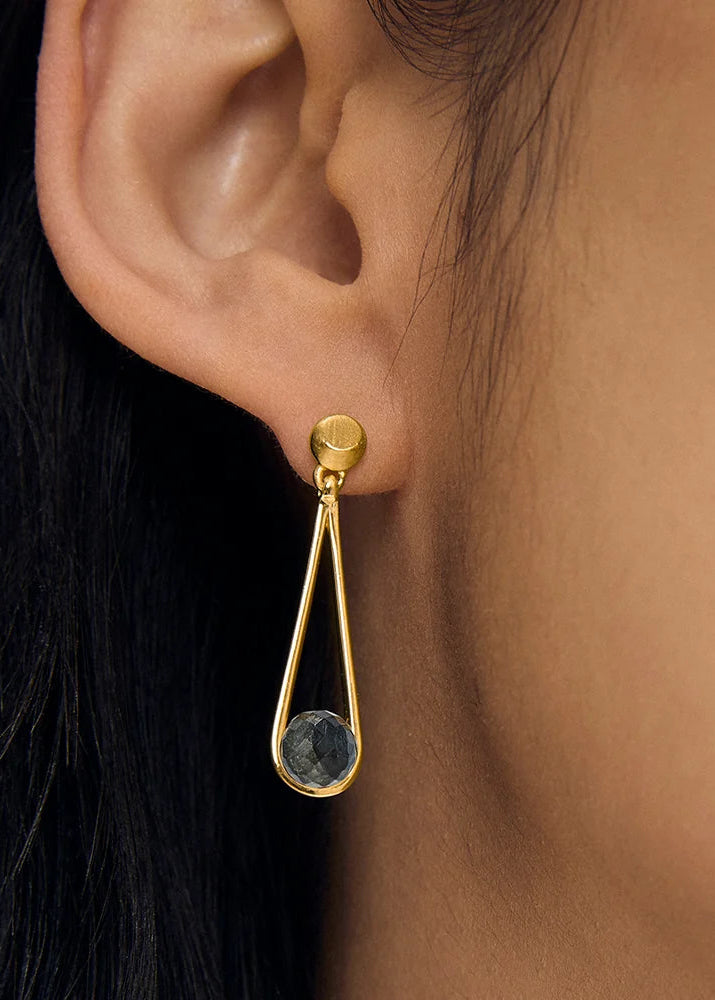 Gold earring with a dark gemstone worn by a person with black hair.