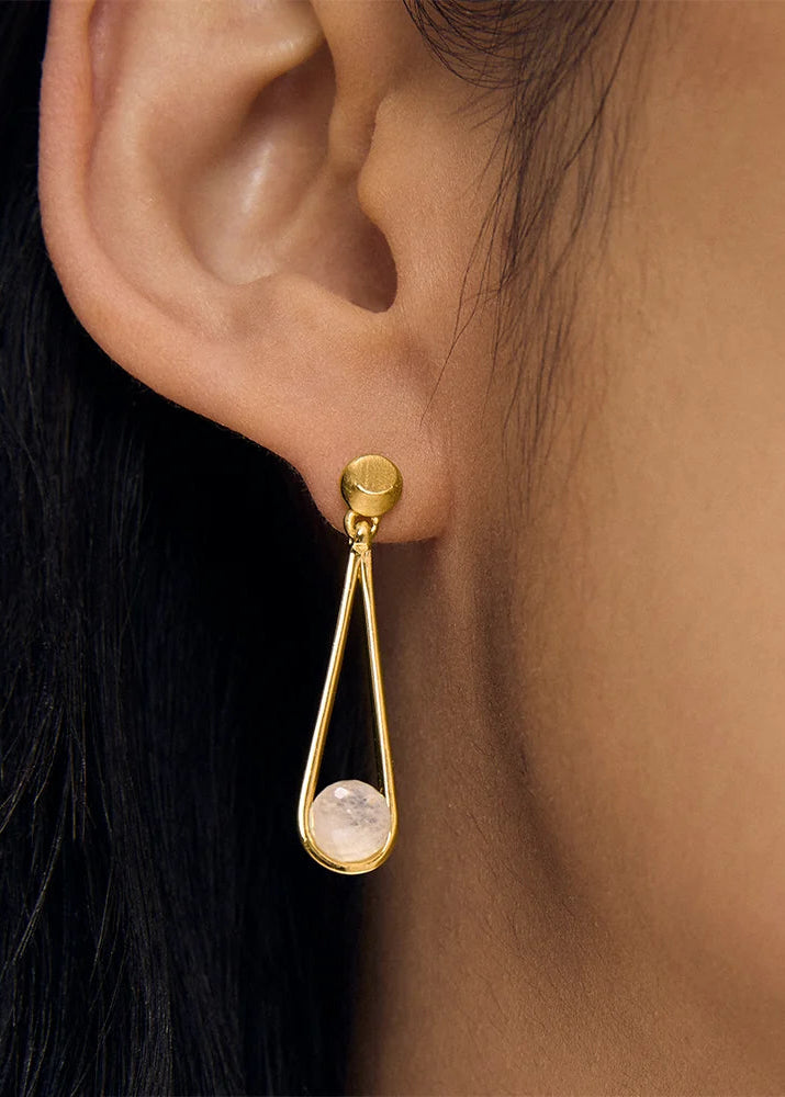Gold earring with a clear gemstone worn by a person with black hair.