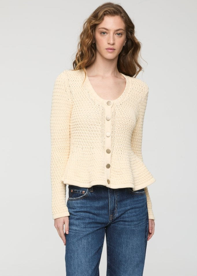 A woman modeling a cream-colored, textured knit cardigan sweater with button-front closure, paired with blue jeans, against a plain light gray studio background.