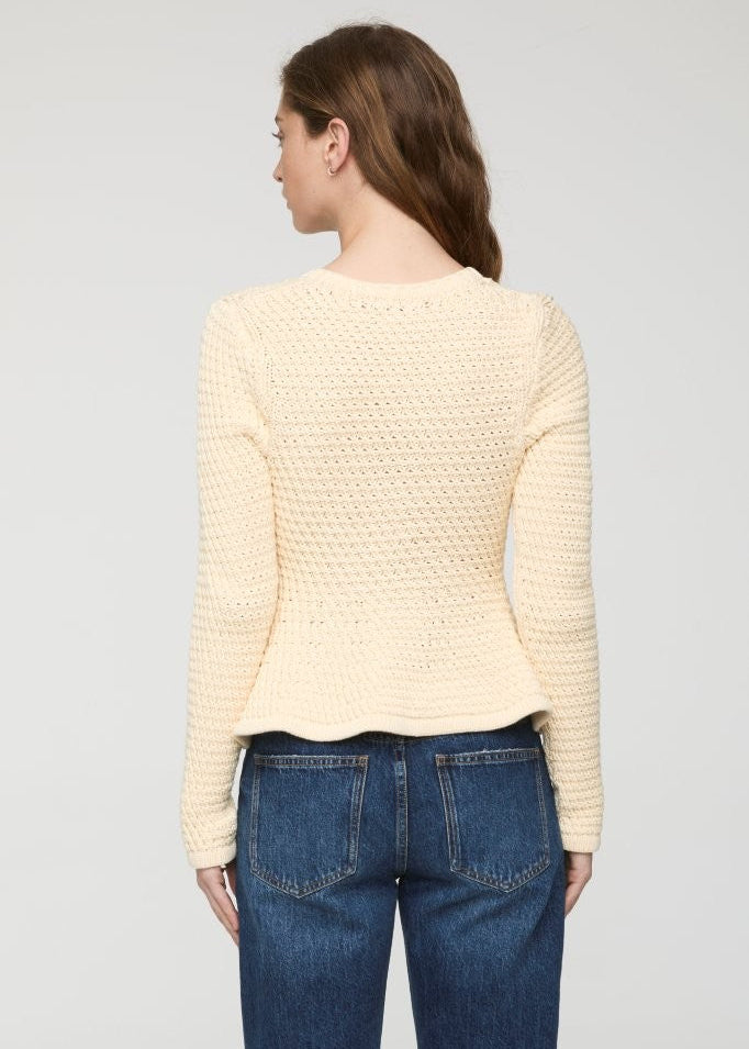 A woman shown from the back wearing a cream-colored textured knit sweater and blue jeans against a light gray studio background.