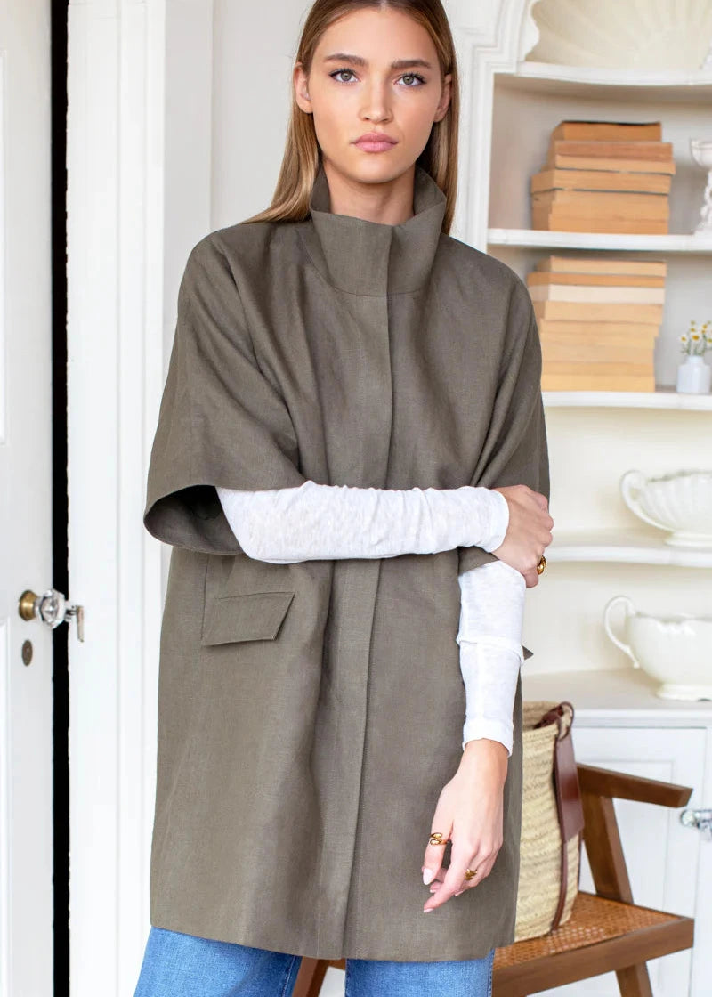 Woman wearing a gray poncho over a white sweater and blue jeans, standing indoors.