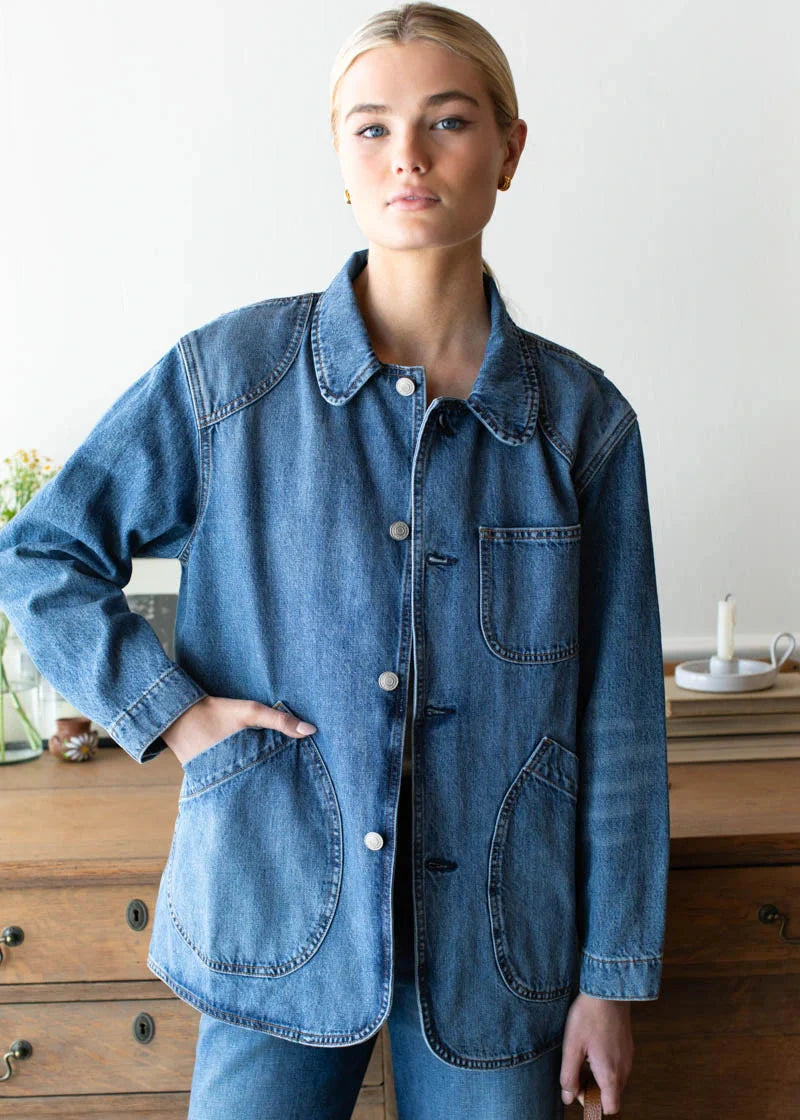 Person wearing a blue denim jacket in a room with wooden furniture.